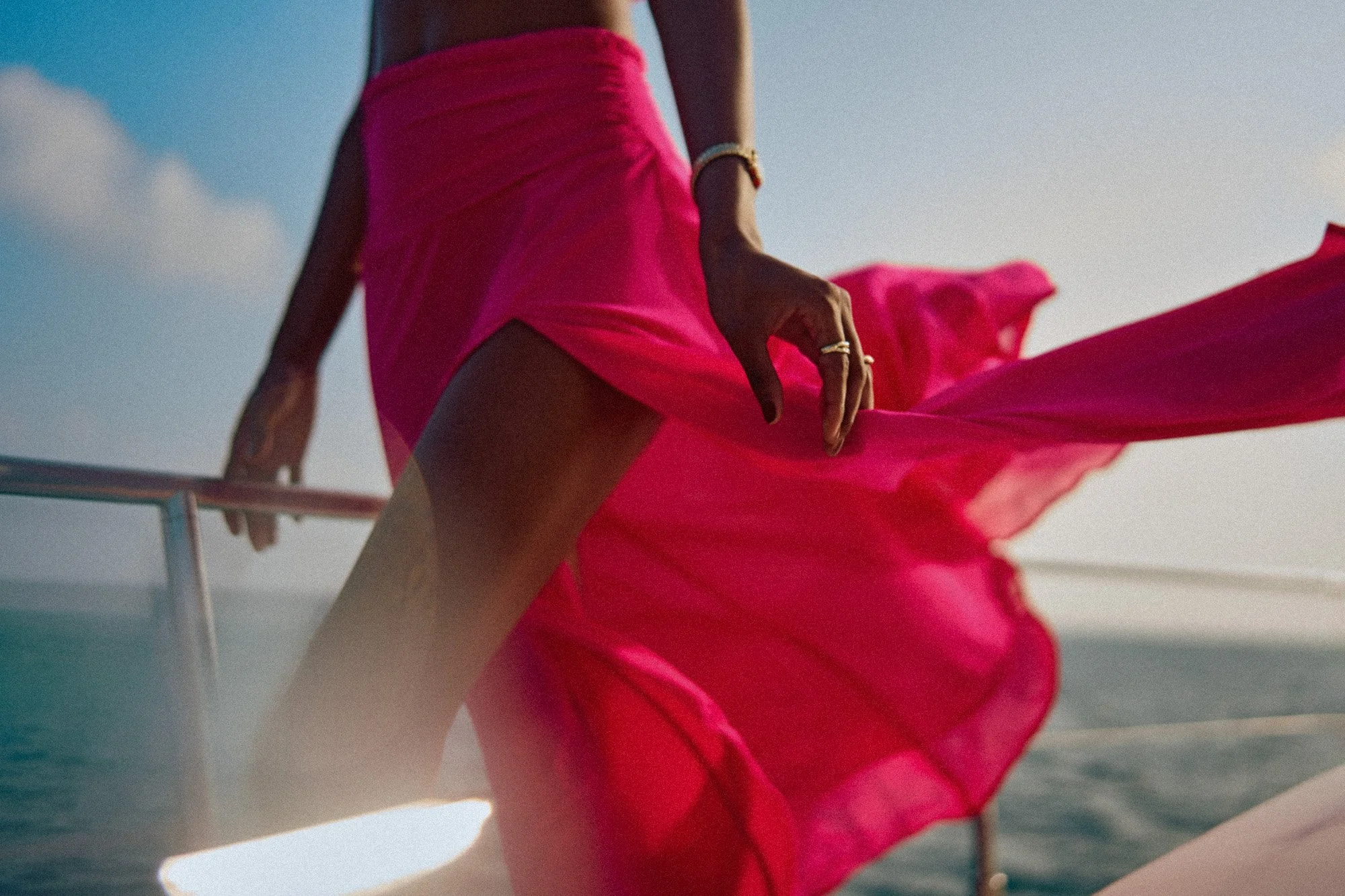 A woman wearing a pink skirt standing on a boat at sea during sunset.