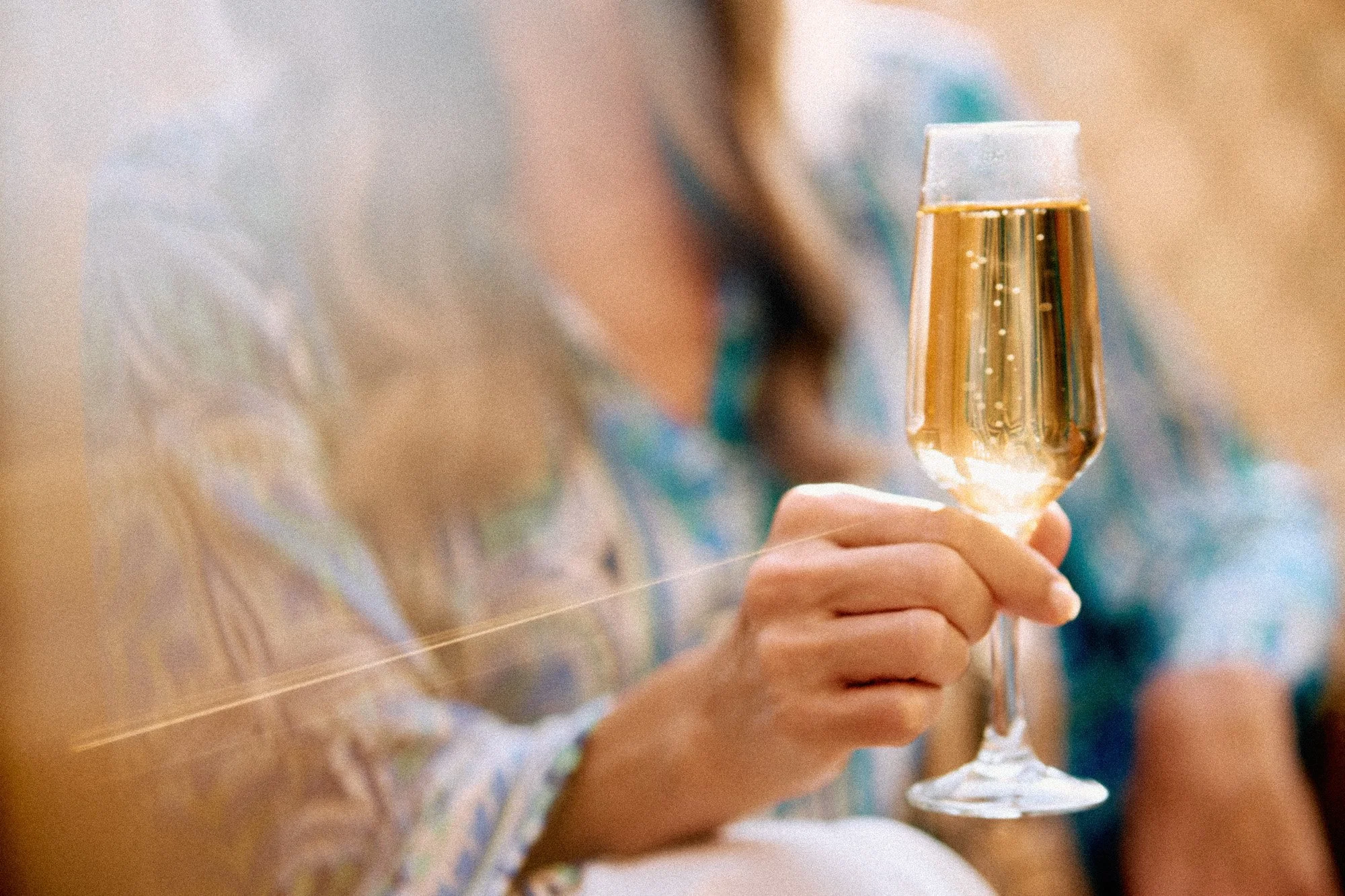 Close-up of a person holding a glass of champagne or sparkling wine at a celebration or gathering.