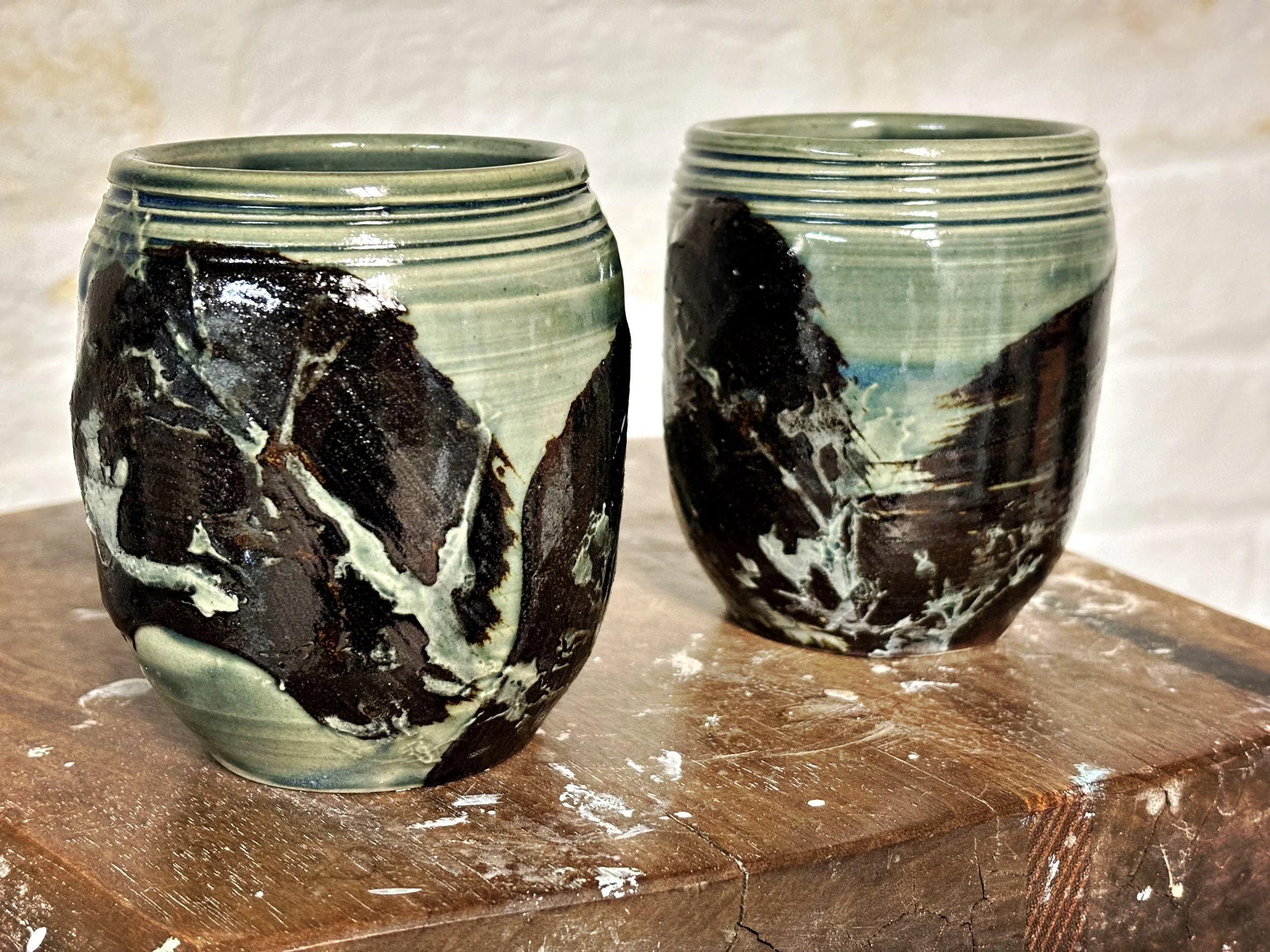 Two decorated ceramic cups on a wooden surface with a light-colored background.