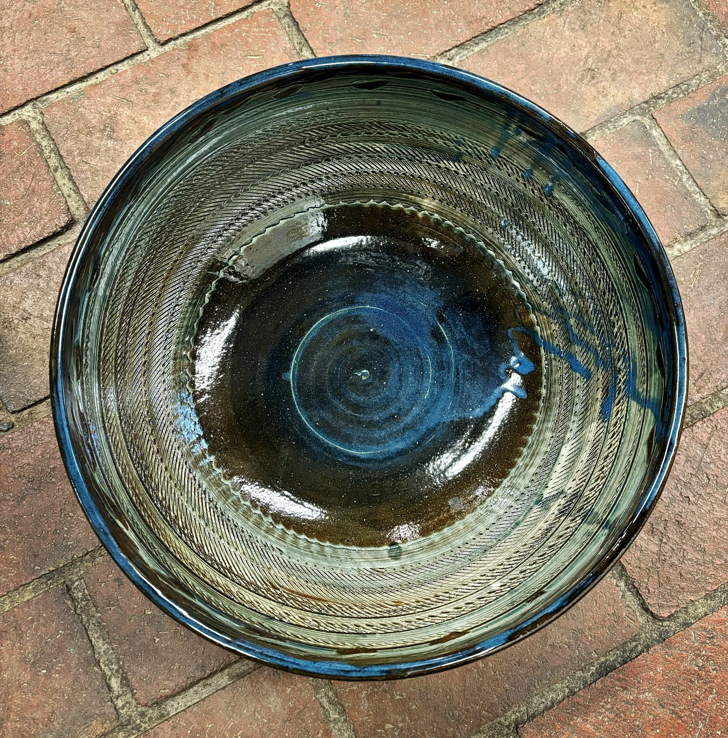The image shows an empty, decorative ceramic stoneware  bowl placed on a brick surface, viewed from above.