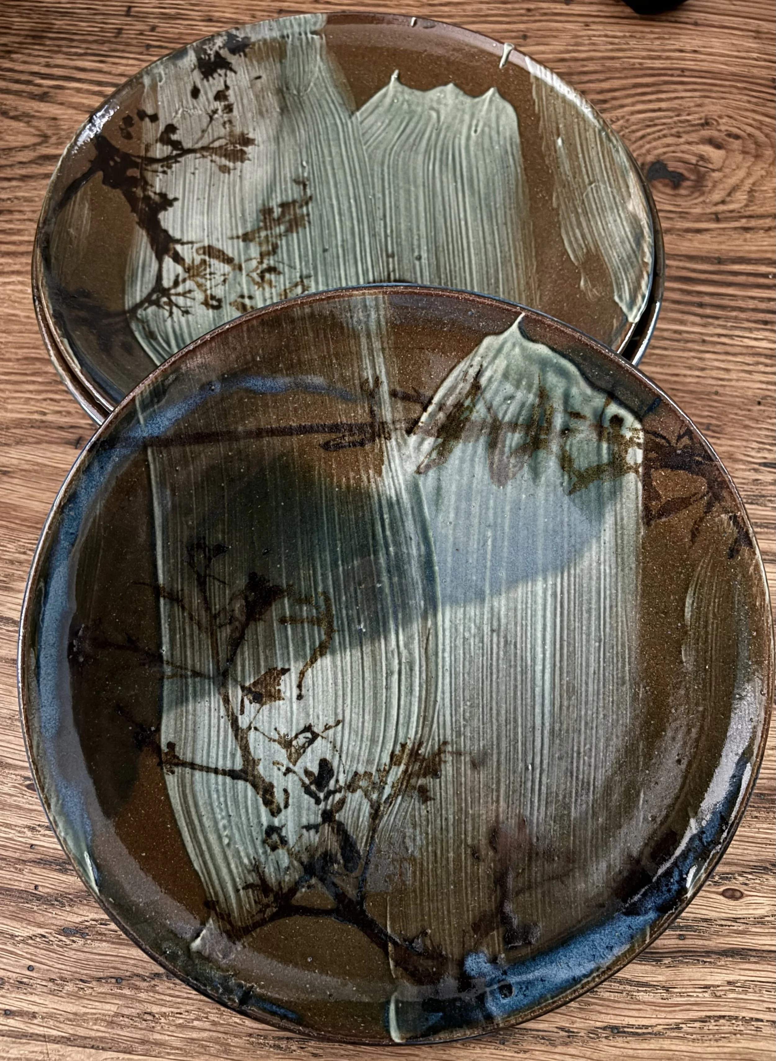 Two ceramic plates with green and brown glaze, placed on a wooden surface.