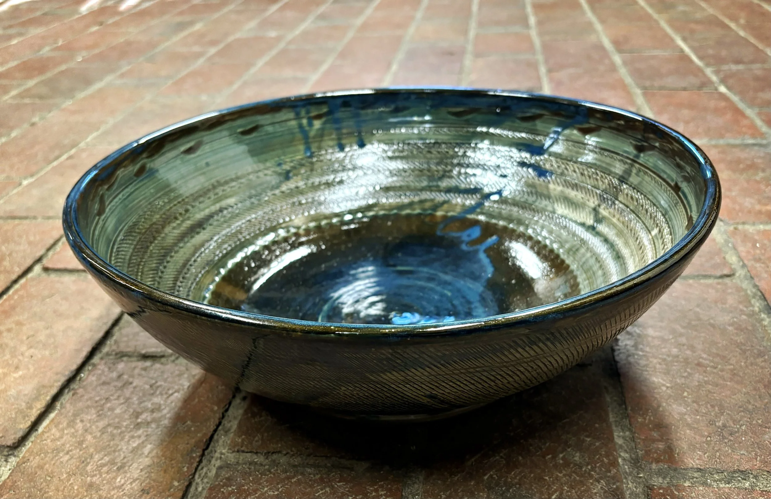 A close-up of a dark ceramic bowl with a glossy interior, sitting on a brick surface outdoors.