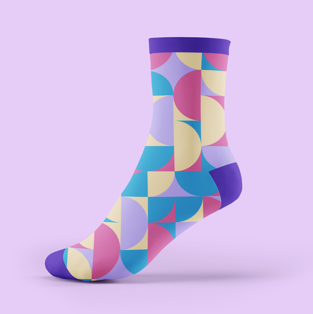 Colorful sock with geometric patterns of circles and squares in pink, yellow, blue, and purple on a light purple background.