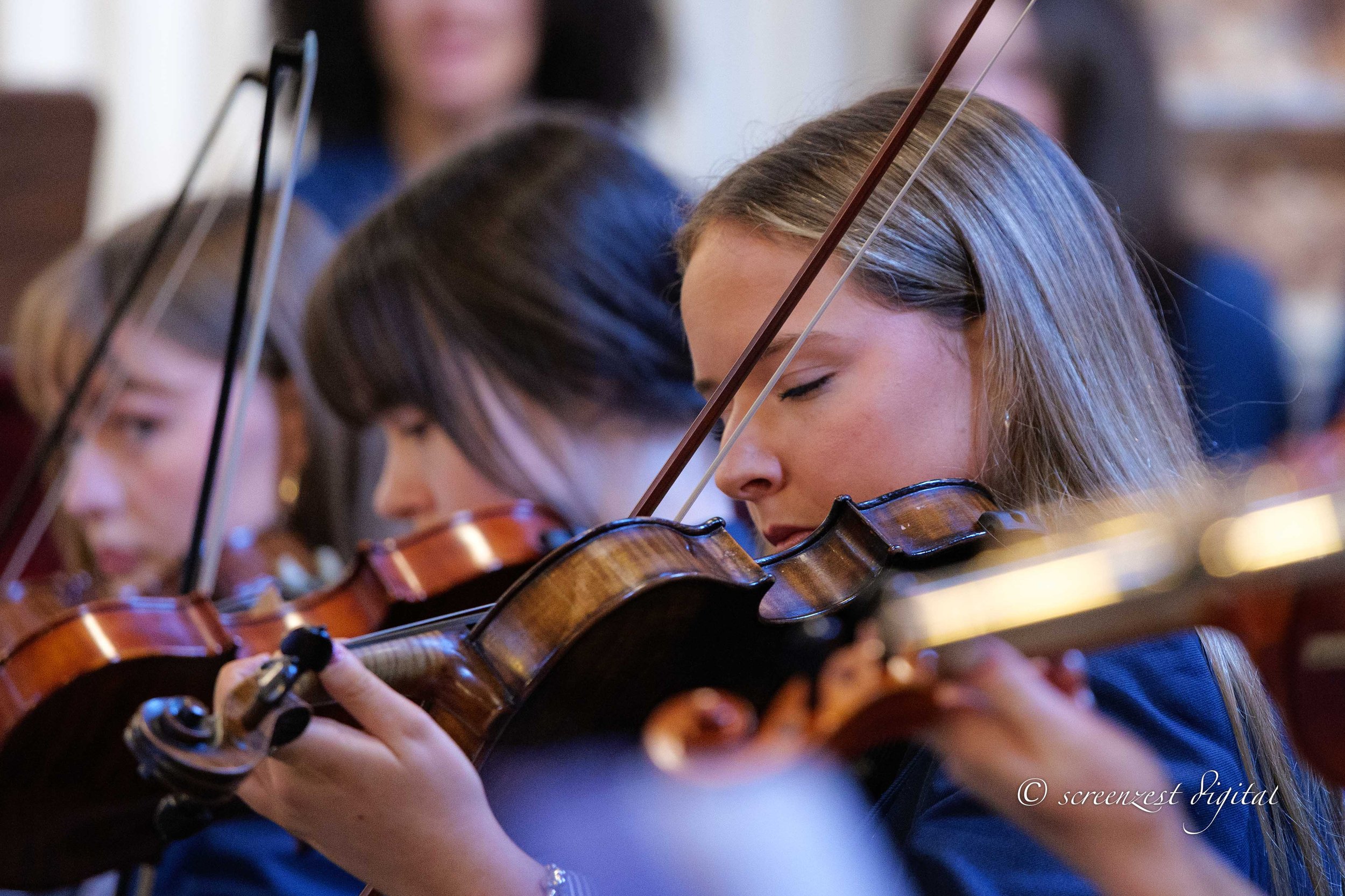 Young woman with closed eyes playing the violin with others in an orchestra