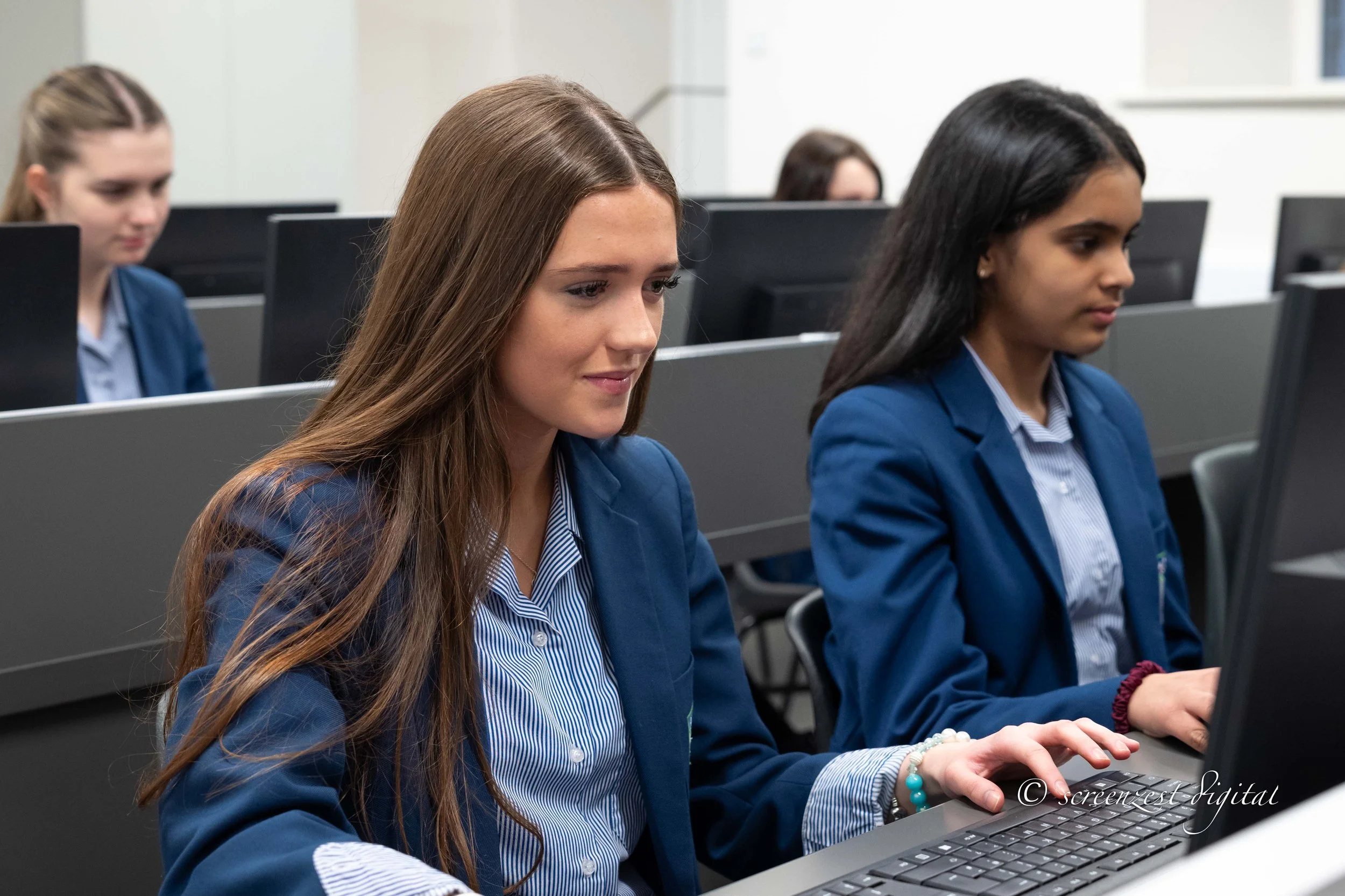 A group of young women in business suits working on computers in a classroom or training room.