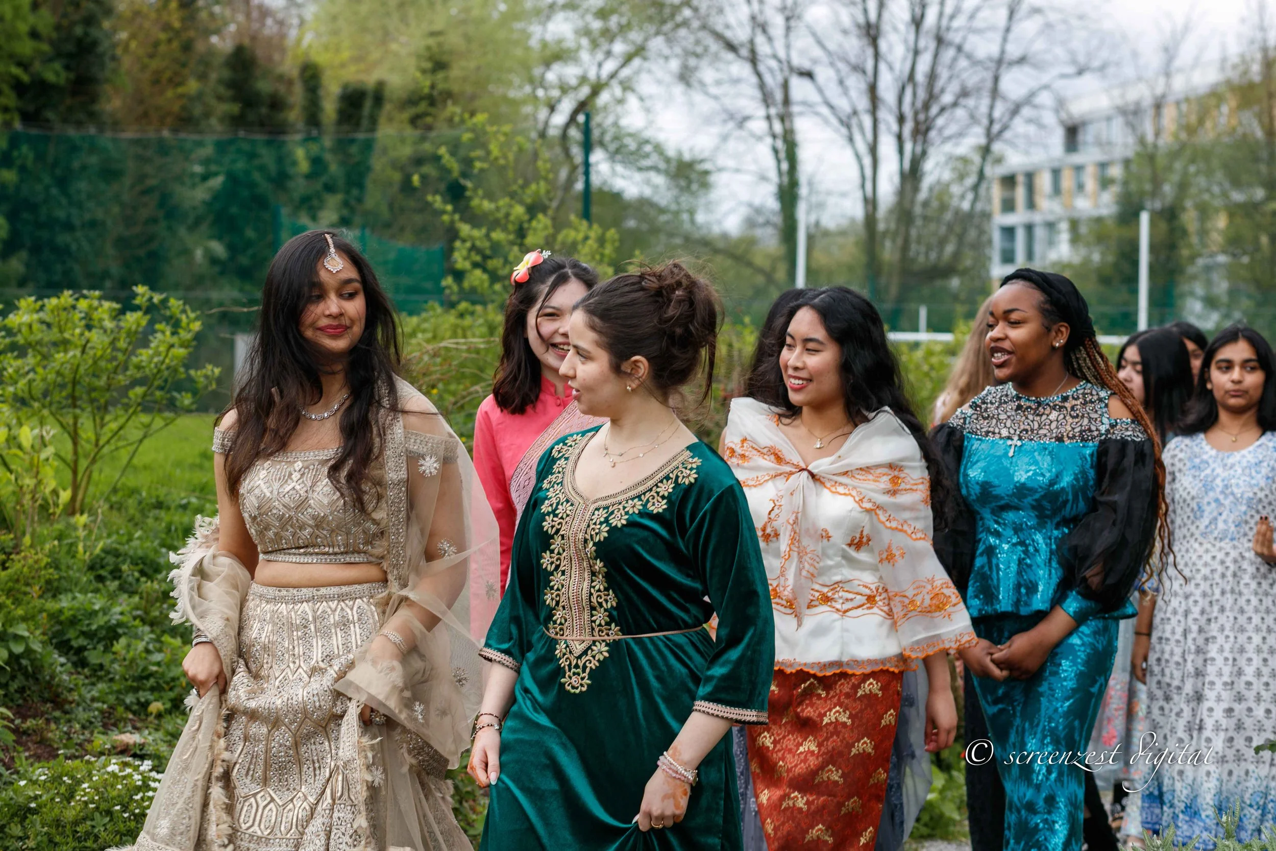 Group of women wearing traditional South Asian attire, walking outdoors in a garden.