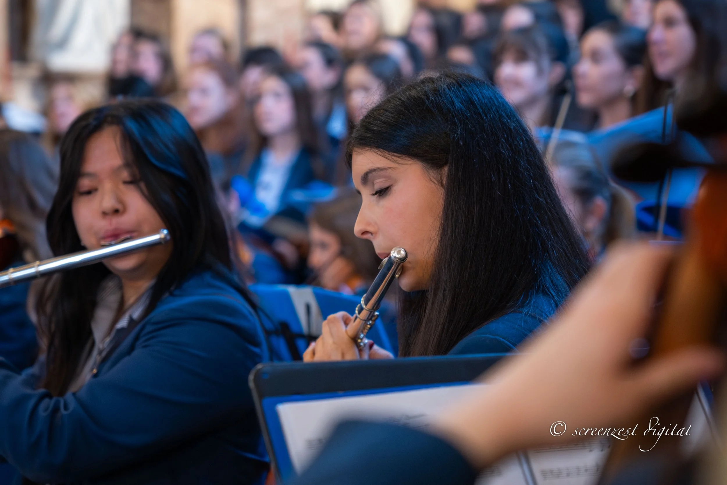 A group of young women wearing blue uniforms playing flutes during a musical performance or rehearsal.