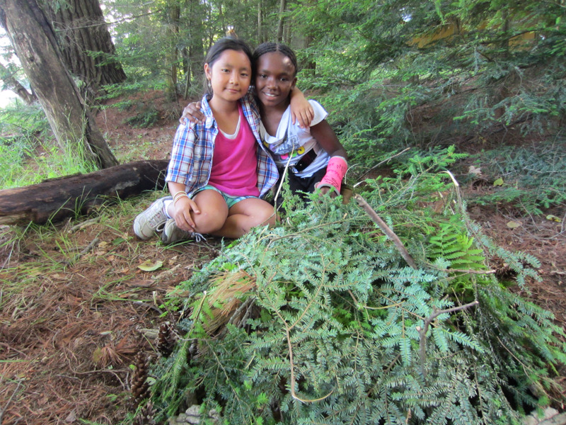 two campers sitting on the ground in the woods with arms around each other