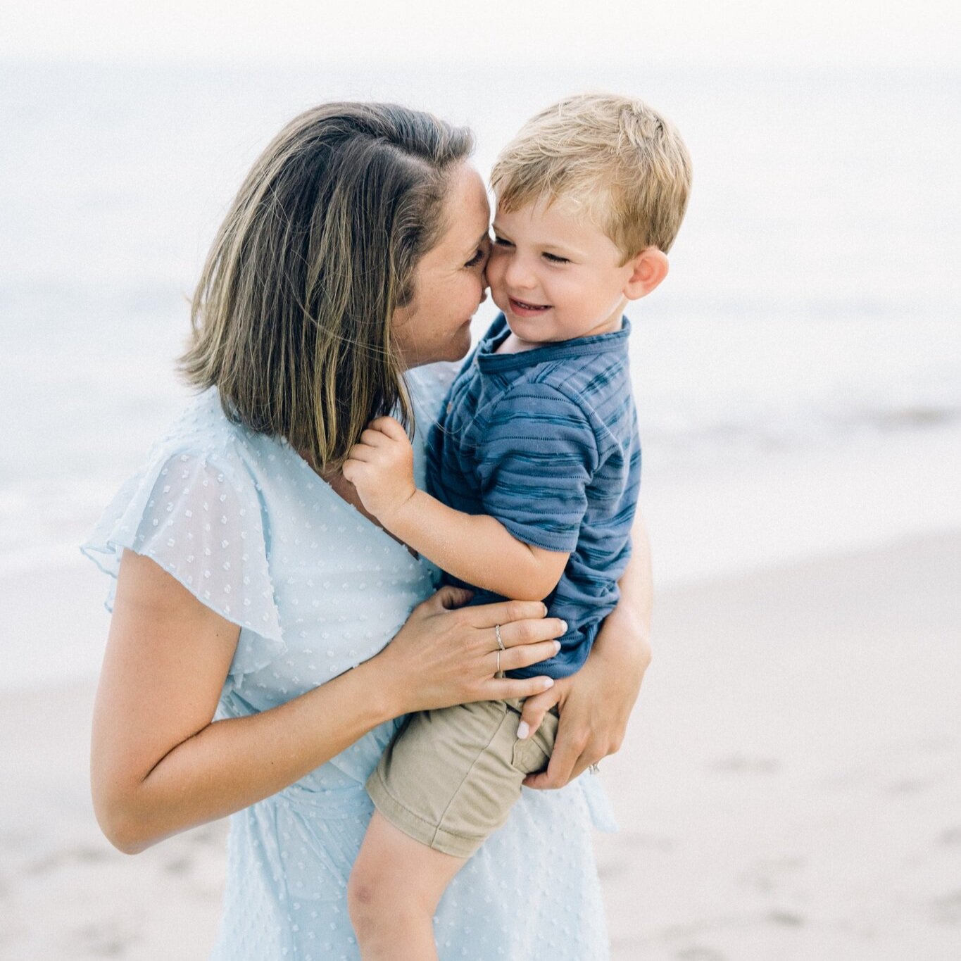 Mother and son cuddle on the beach during a family photo session in Bethany Beach, DE with AnneMarie Hamant