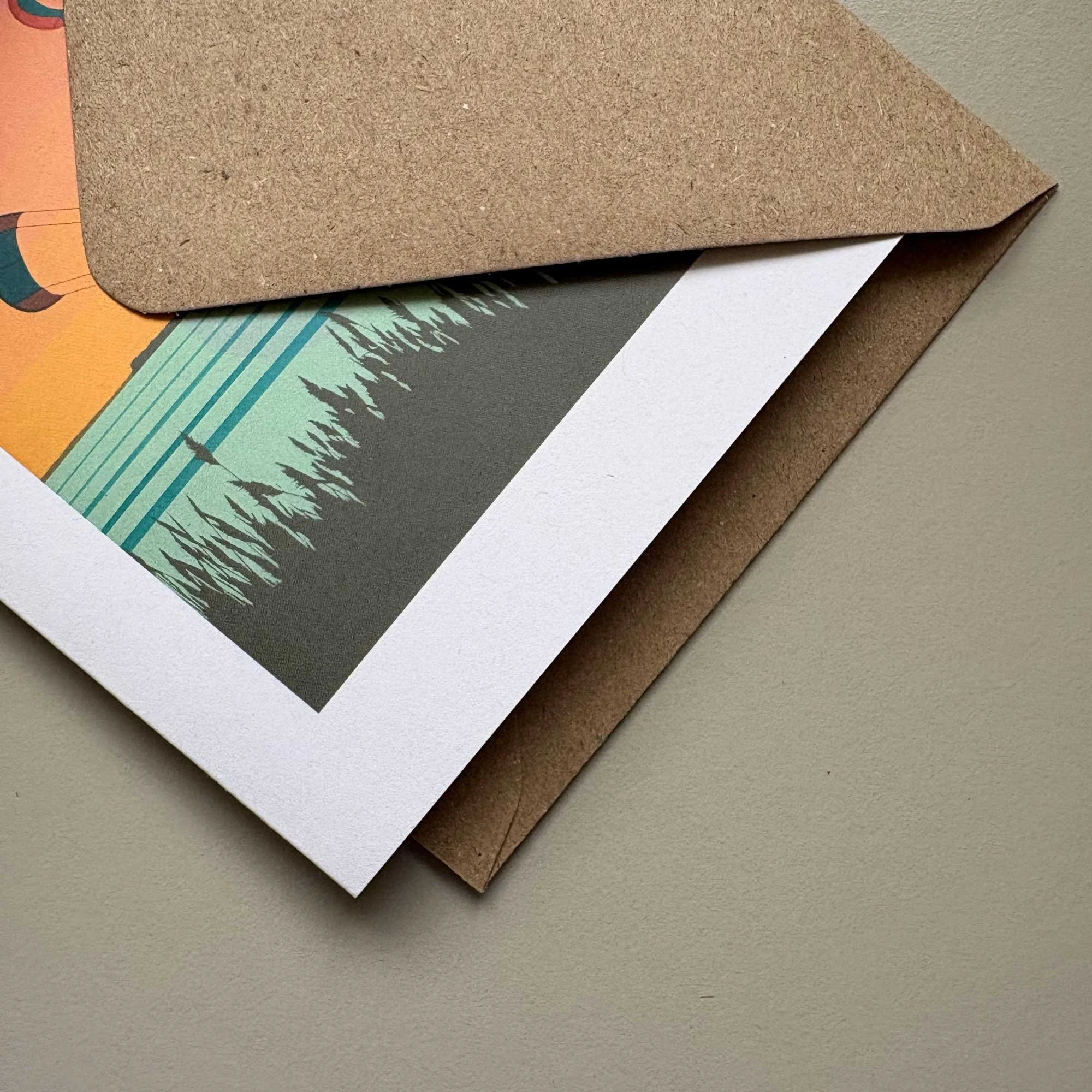 Close-up of a printed photograph partly inside a brown envelope, showing part of a mountain landscape with trees and sky.