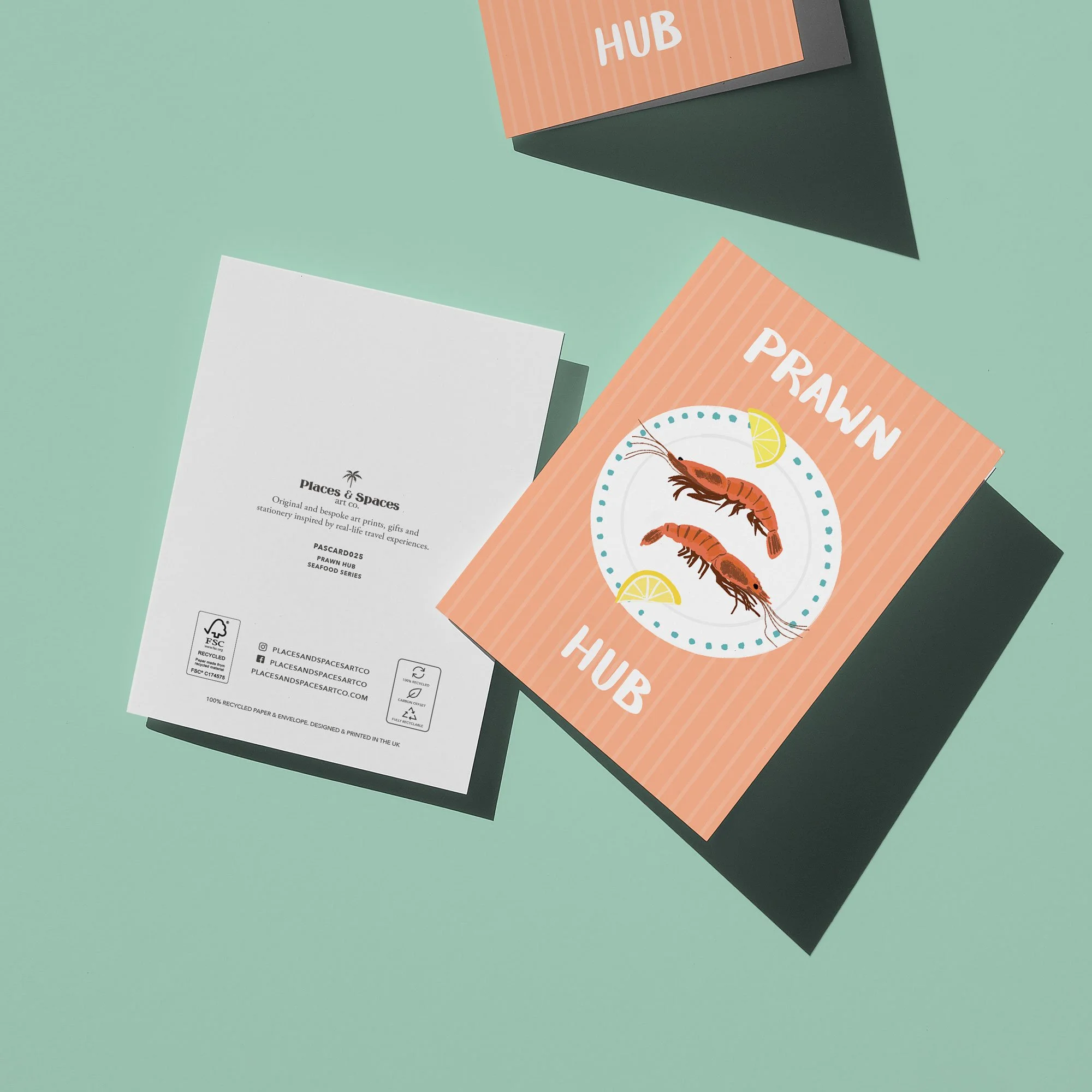 Two folded cards on a mint green background, one with the text 'Prawn Hub' and an illustration of prawns with lemon wedges, the other with white text on a black background that is partially visible.