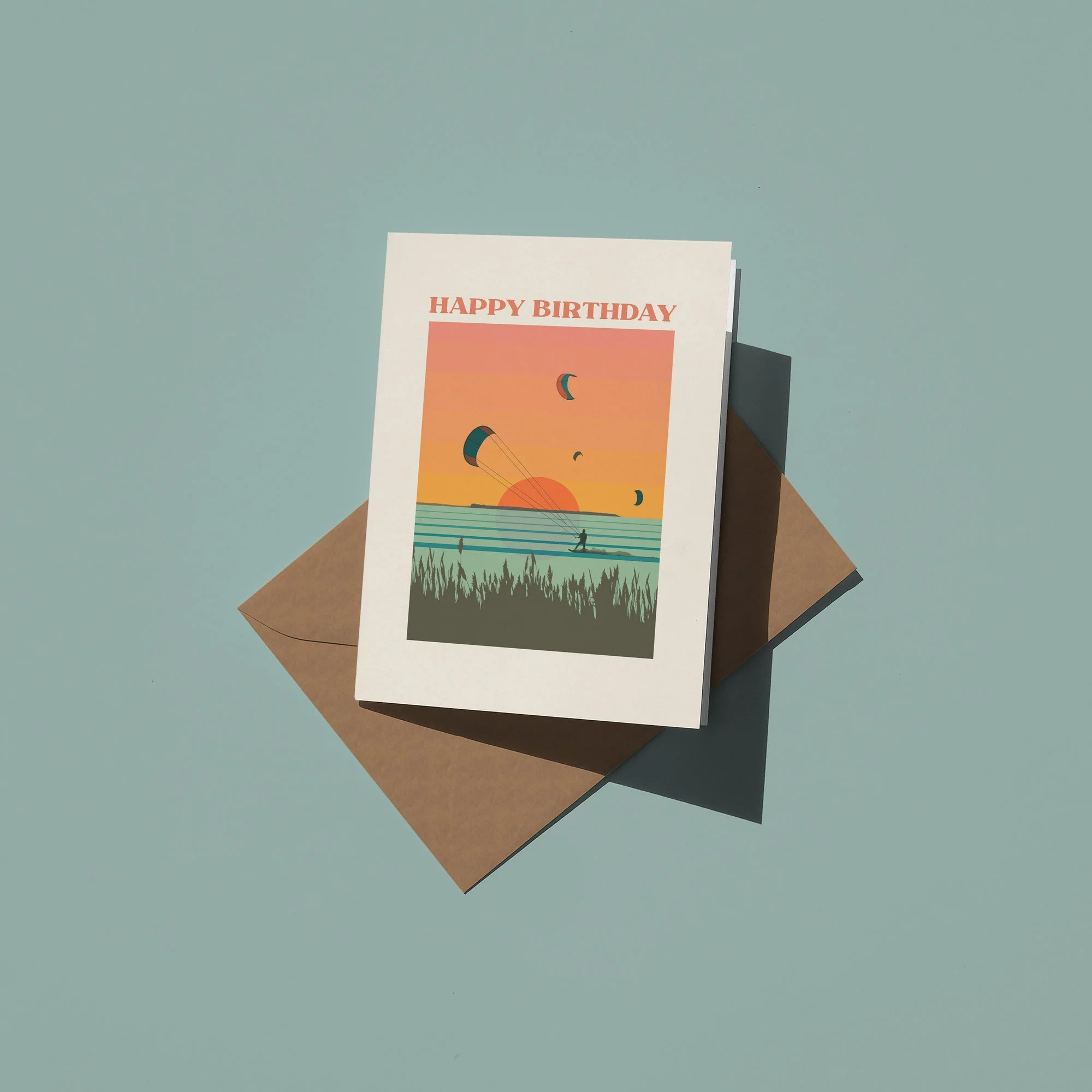 A birthday card with a sunset scene, featuring parachutes, a person kite surfing, and the text "Happy Birthday" on top.
