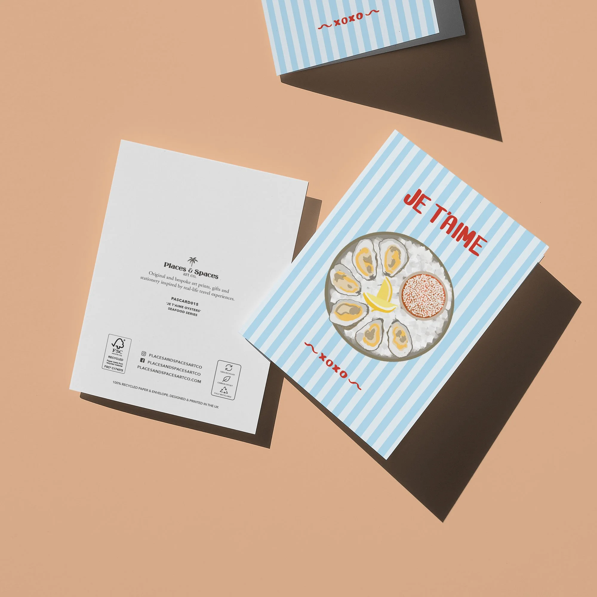 Flat lay of a seafood menu and a white card from Places & Spaces against a peach background. The menu has a blue and white striped pattern with red text saying 'JE T'AIME' and an illustration of oysters on ice with lemon and roe.