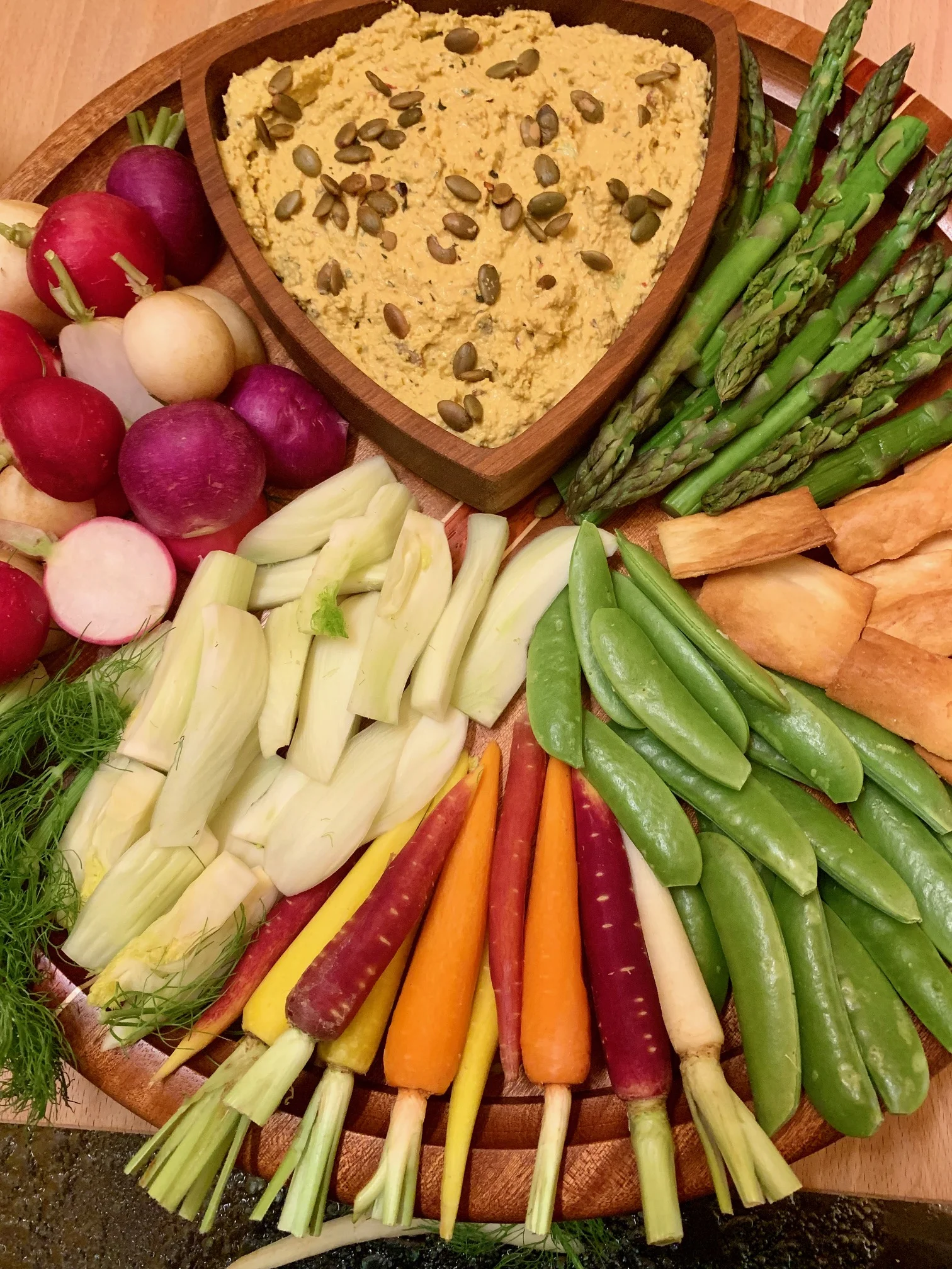 Serve with pita chips and assorted veggies. Pictured here rainbow radishes, fennel, rainbow carrots, sugar snap peas, pita chips and cooked asparagus.