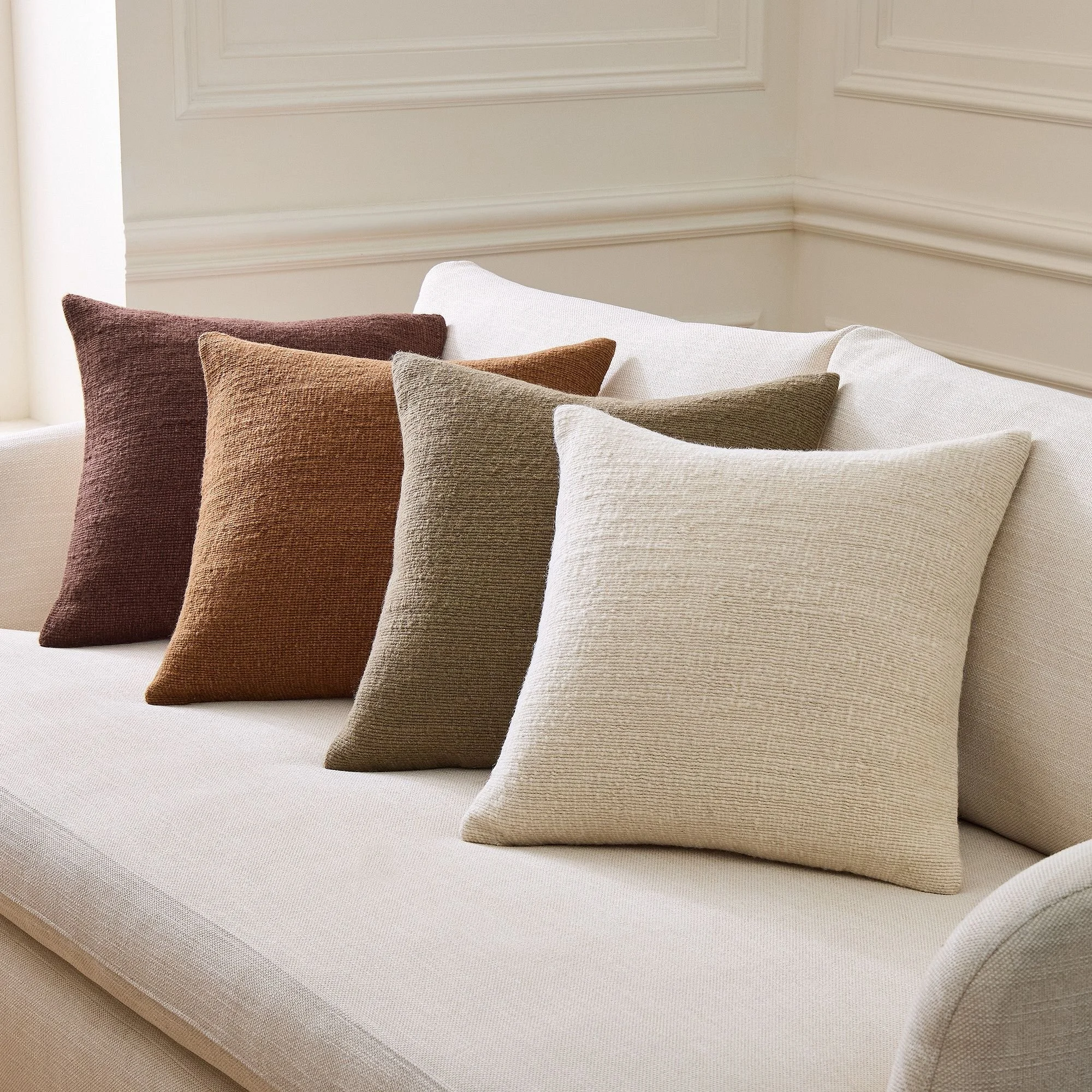 Close-up of several decorative throw pillows on a cream-colored sofa, with a beige wall with molding in the background.