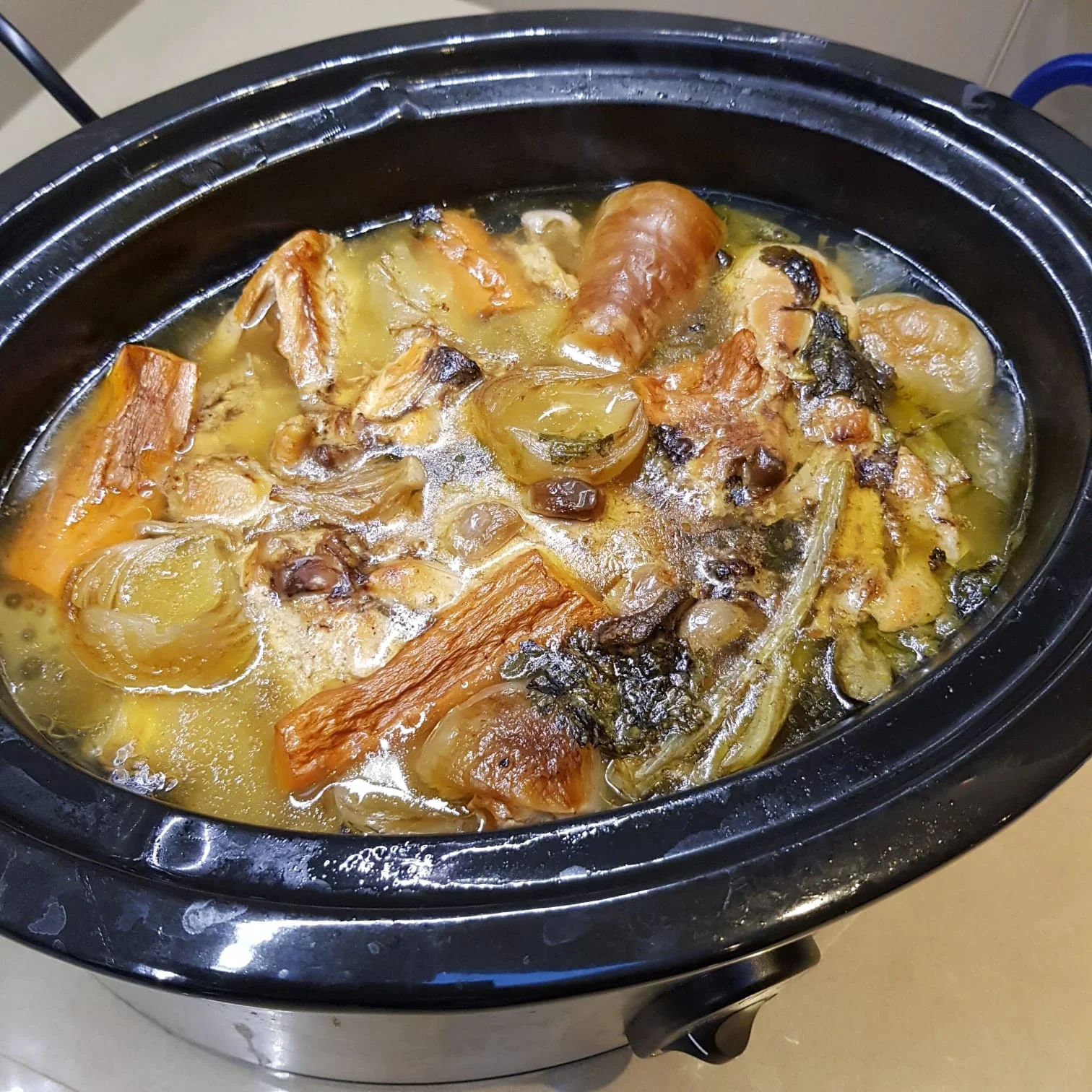 Cooked bone broth with beef and vegetables in a slow cooker, rich in collagen and nutrients for joint and bone health.
