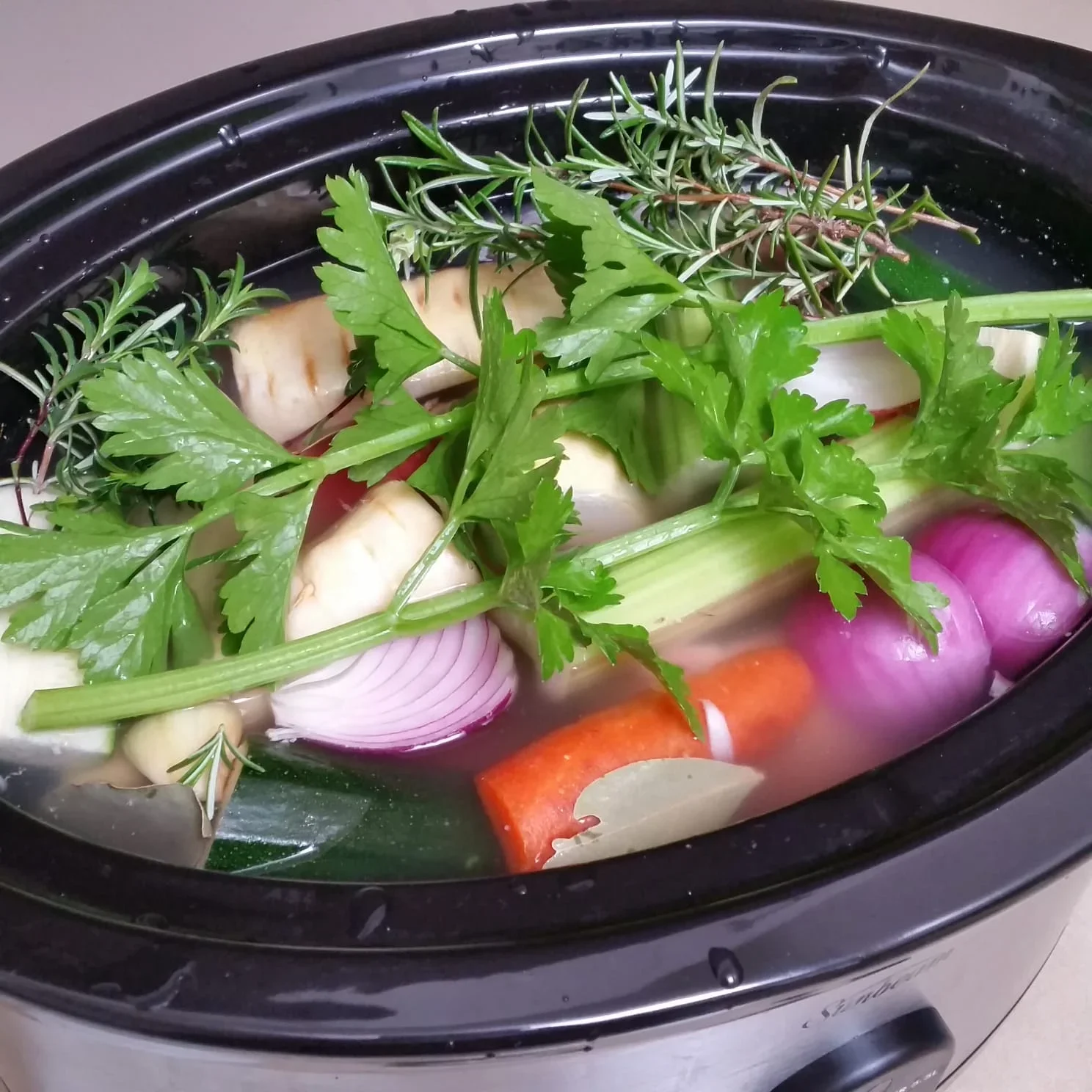 Fresh vegetables, herbs, and bones simmering in a slow cooker to make collagen-rich bone broth for older adults.