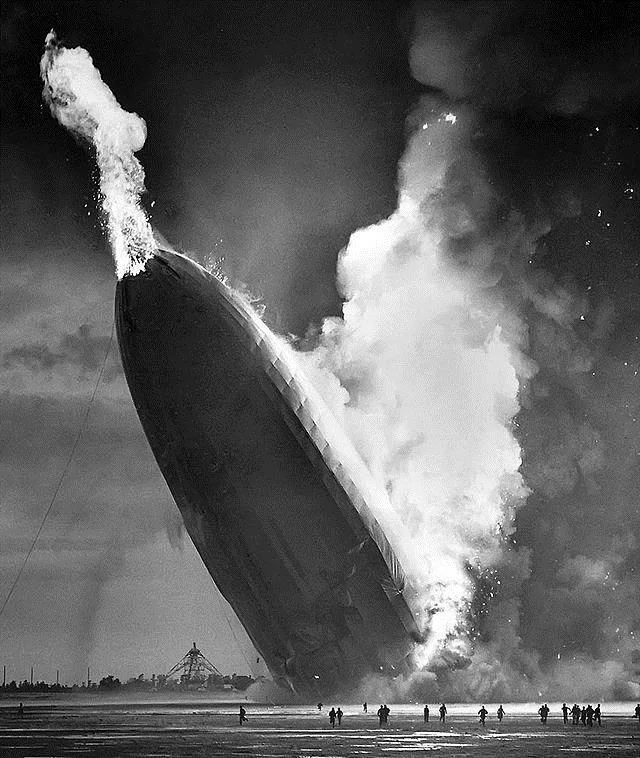 As the hydrogen gas burned and escaped from the rear of the Hindenburg, the tail dropped to the ground sending a burst of flame punching through the nose. The ground crew below scatters to flee the inferno (photo courtesy AP)