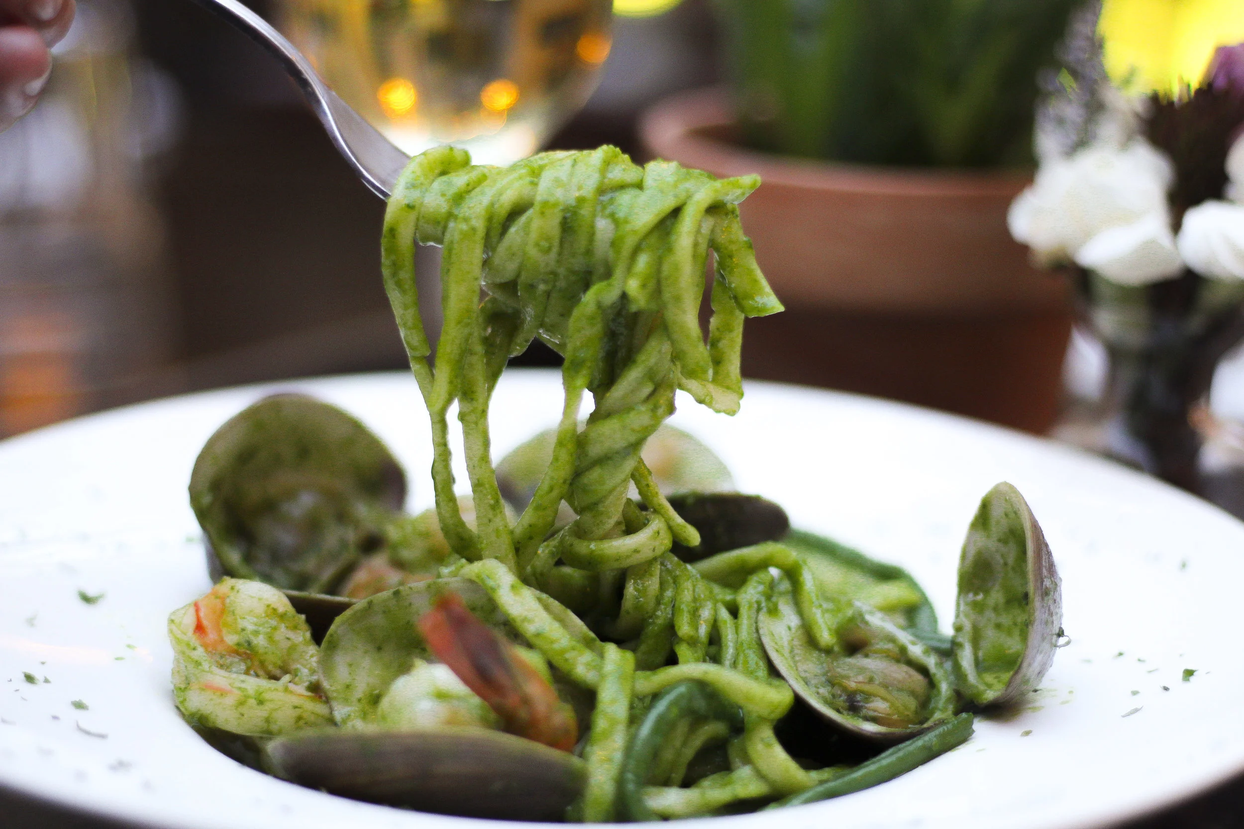 Close-up of green pasta with clams on a white plate.