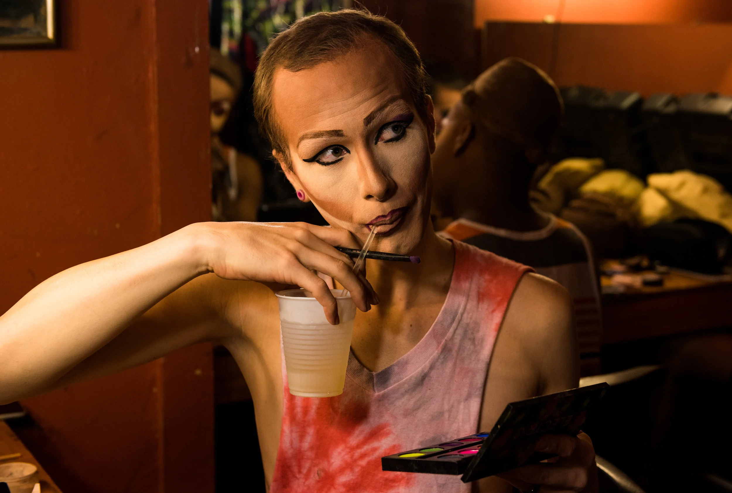 Looking up at another queen, Koedam pauses his eyeshadow application to take a sip of his drink.