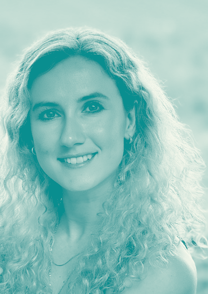 A woman with long curly blonde hair smiling outdoors.