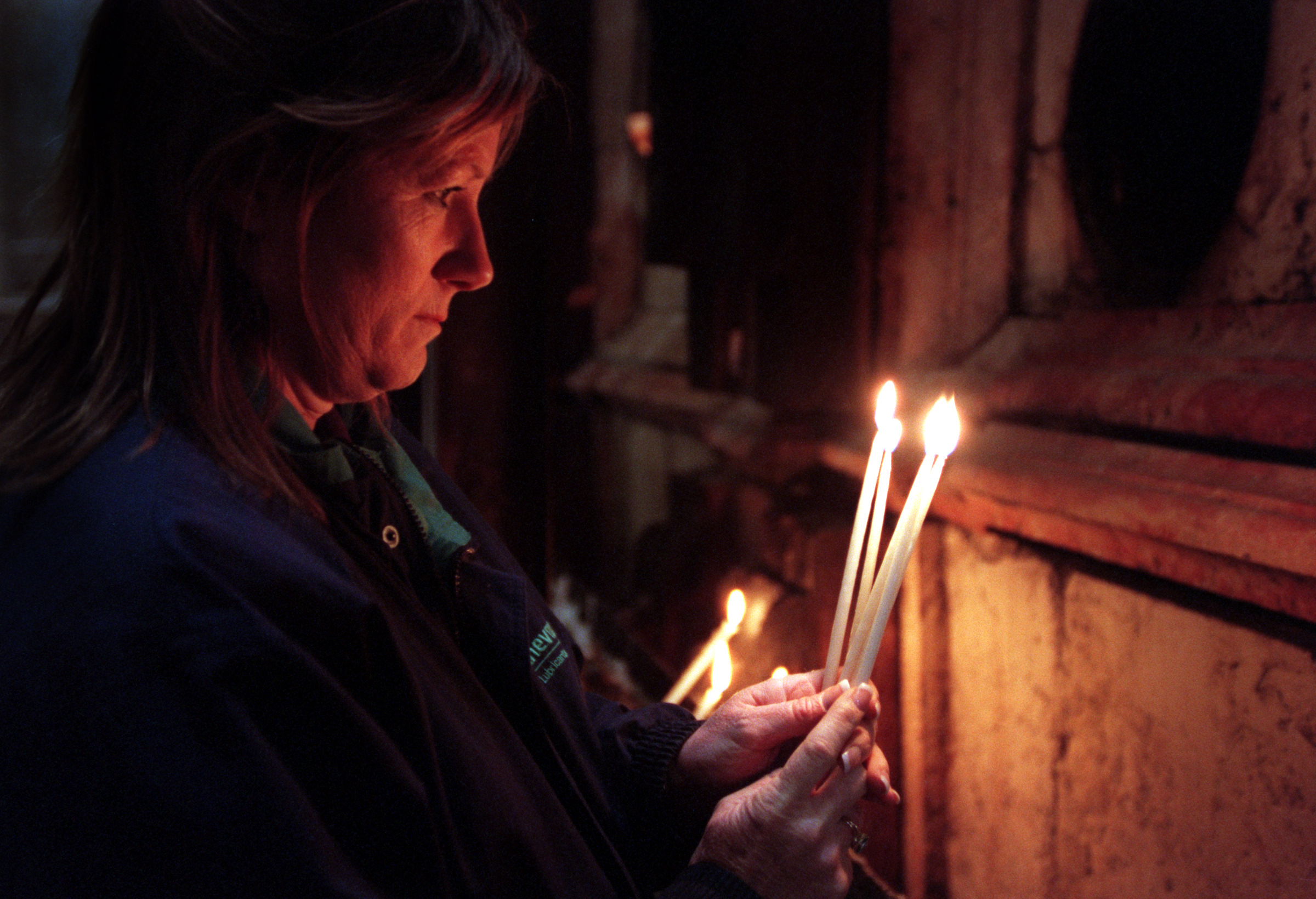 Interfaith member Melinda Griffith prays for sick family members and lights candles at Christ's tomb in the Church of the Holy Sepulcher, site of Christ's death, burial and resurrection, in the Old City of Jerusalem. ©Gail Fisher Los Angeles Times