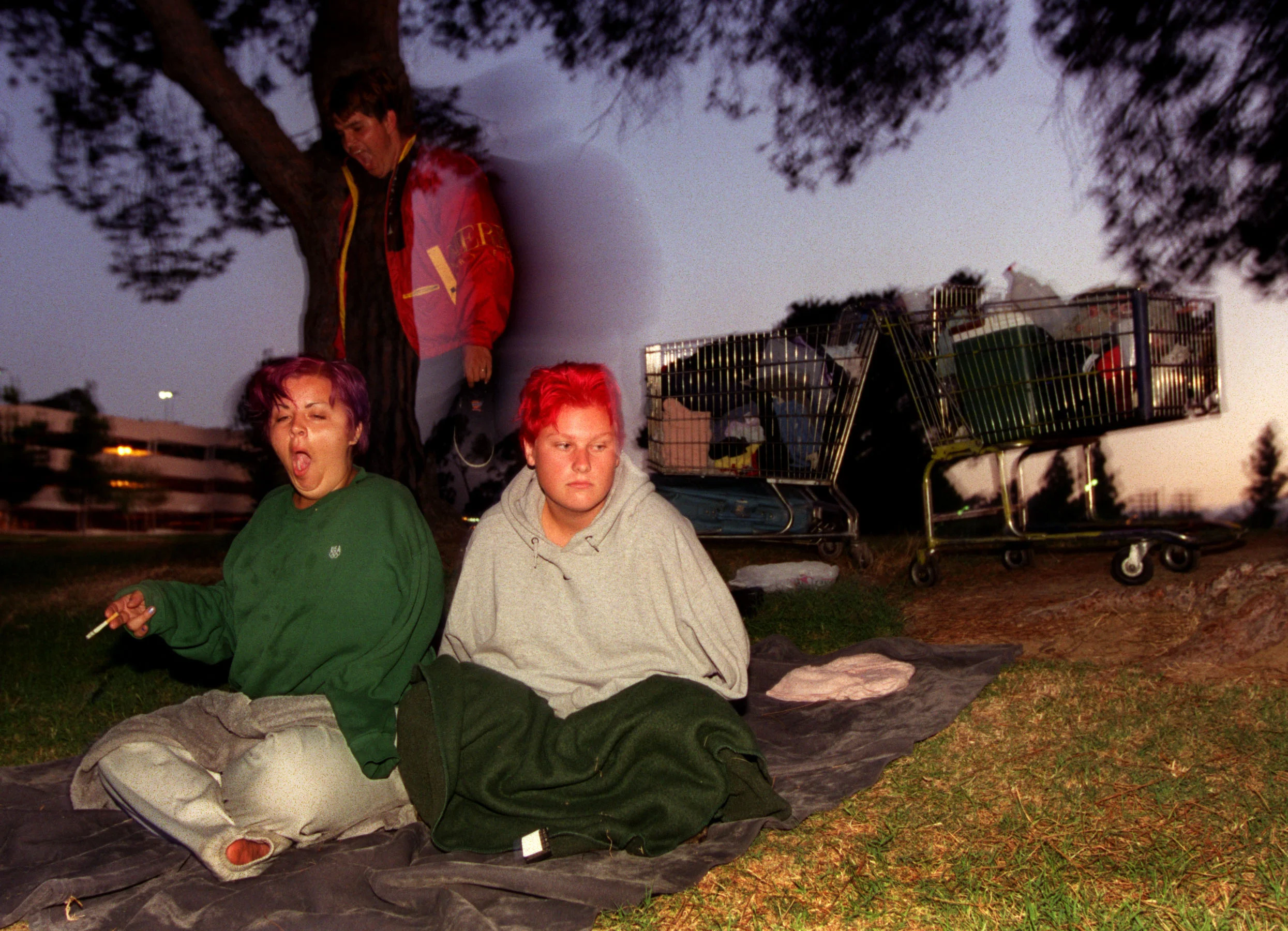 Wrapped in sweatshirts and blankets against the cool summer morning, Janea right, and her friends Dianna and Matt Dewey adjust to their new home with amazing ease. Wedged between East LA's municipal court, the freeway and a Sheriff's station, Belvedere Park, located on a few grassy acres, is where they are squatting these days. ©Gail Fisher Los Angeles Times 