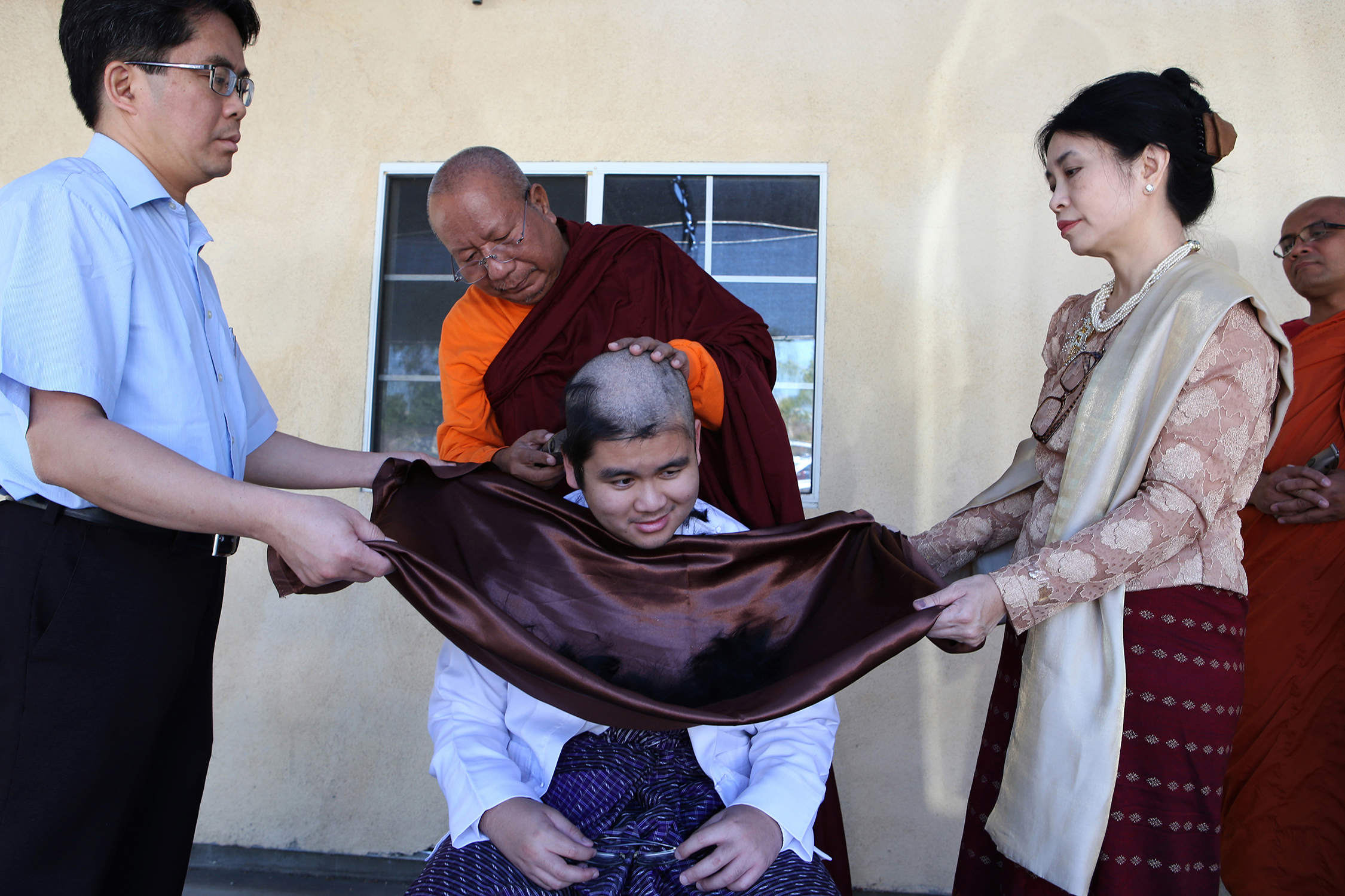  USC student Robert Win Maw Min, 20, recently checked in for a three day stay at the Dhammajoti Meditation Center in Baldwin Park. His head is shaven by Ashin U Uttama as part of the experience. Flanking the young man are his parents, Dr. Tin A Than,
