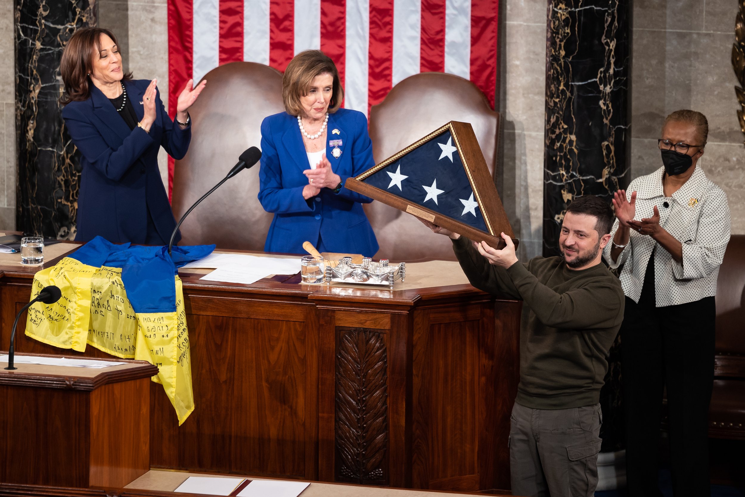  After addressing a joint session of Congress, Ukraine President Volodymyr Zelenskyy holds up a U.S. flag gifted to him by House Speaker Nancy Pelosi (D-Calif.) while Pelosi and Vice President Kamala Harris applaud a joint session of Congress in the 