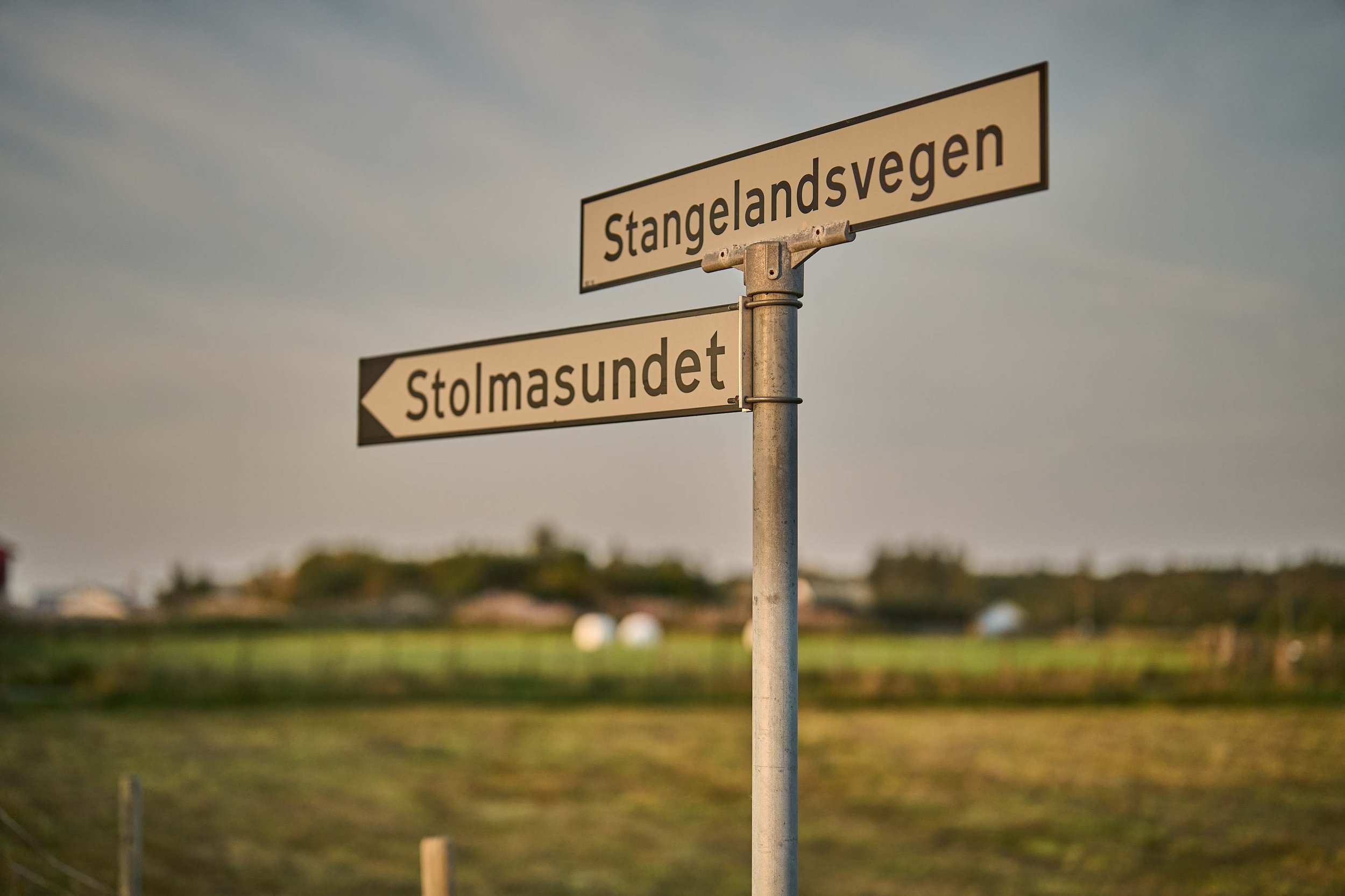 Tremåls skilt som peker mot Stangelandssvegen, Stolmasundet og et ukjent område, med en åpen landskap i bakgrunnen.