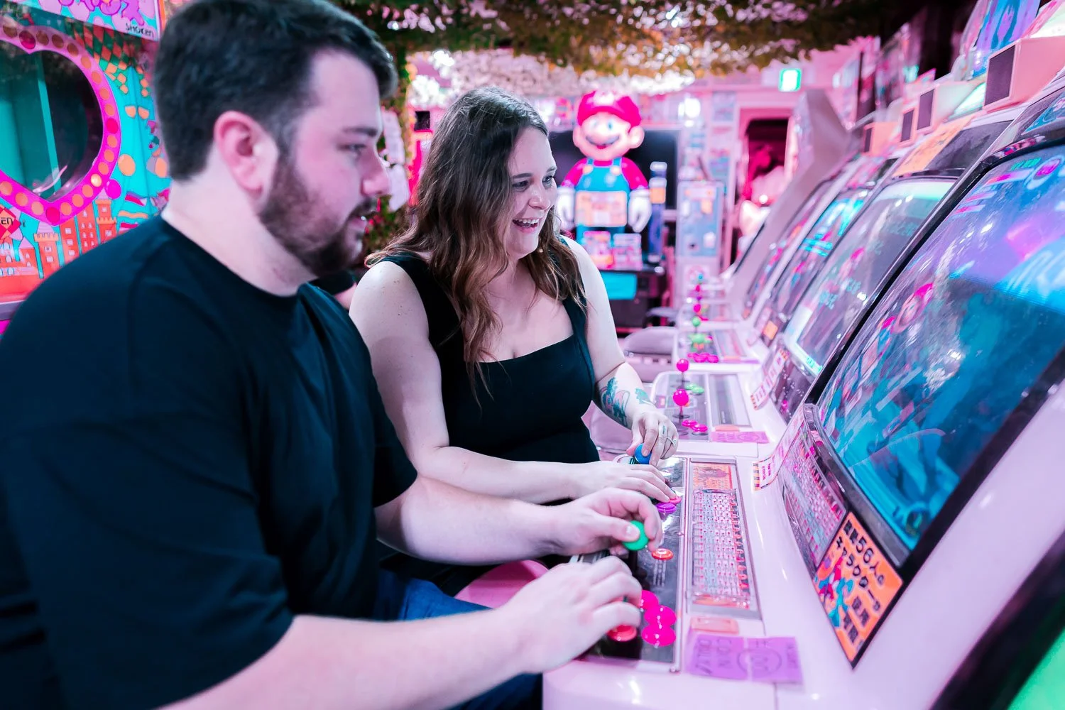 Couple playing a retro arcade game together in a neon-lit Akihabara arcade during their Tokyo honeymoon photoshoot