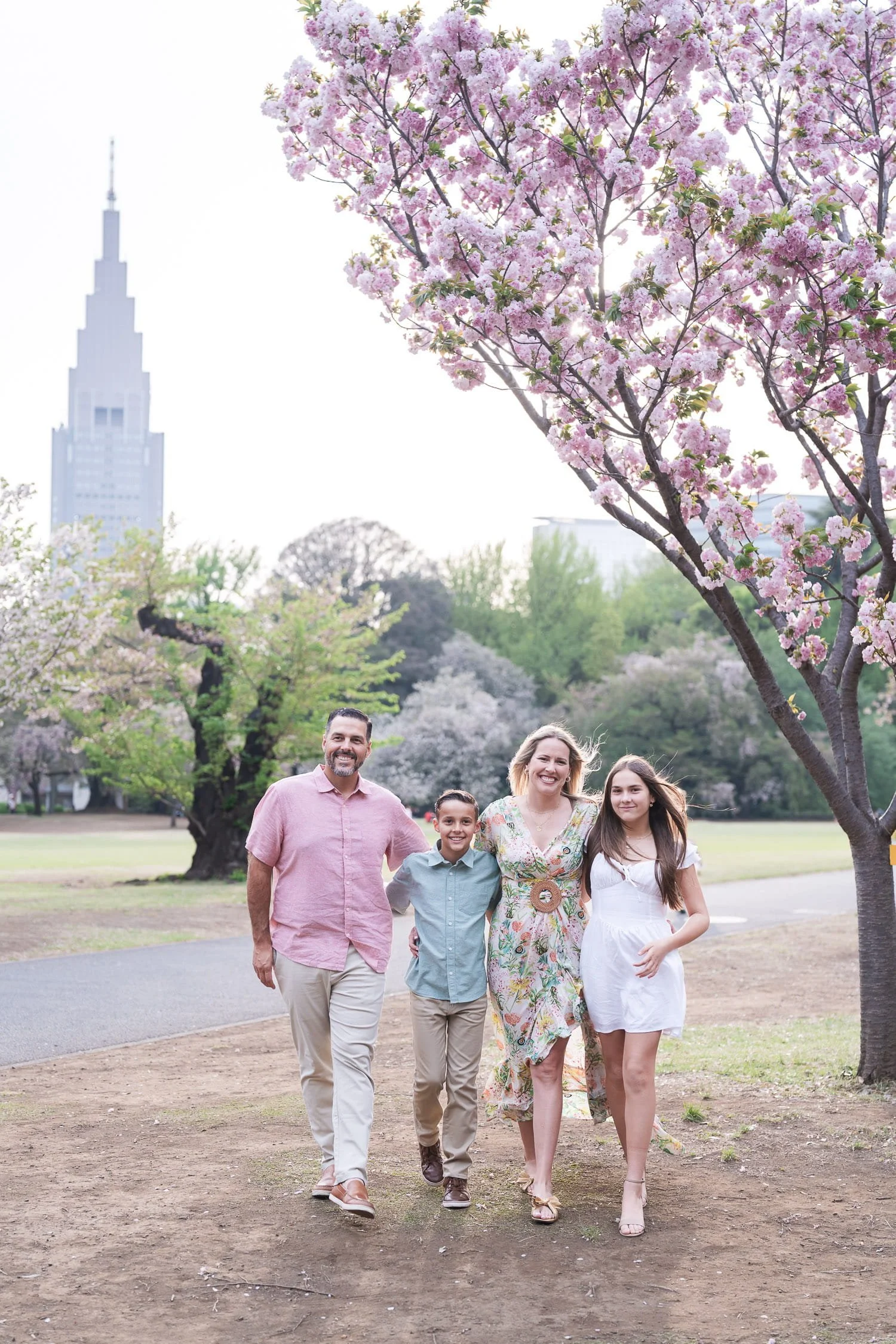 Jeffrey's family strolling under sakura trees with NTT Tower background, captured in Shinjuku Gyoen National Park