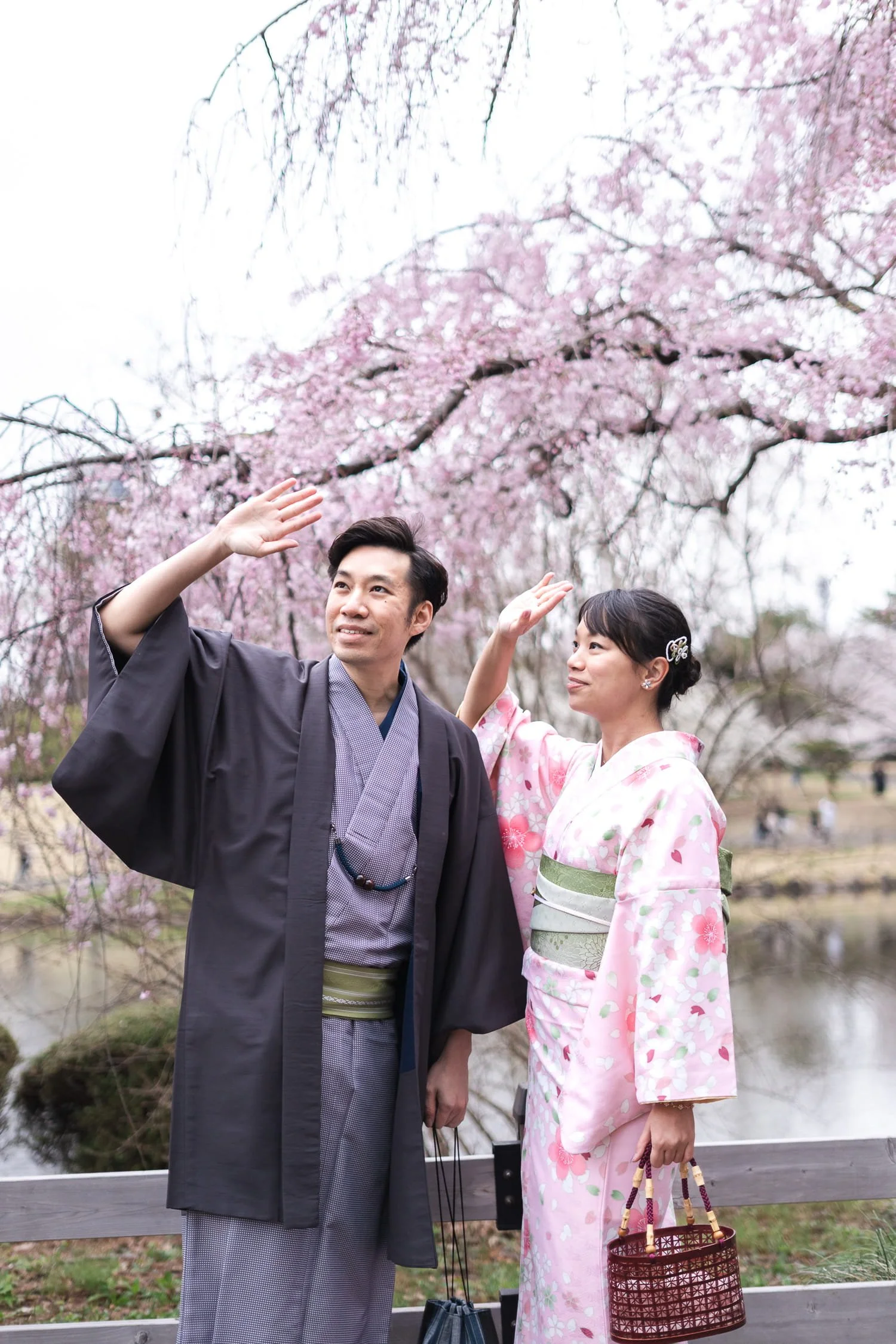 The couple raised their hands to block the sun while standing in front of pink sakura tree