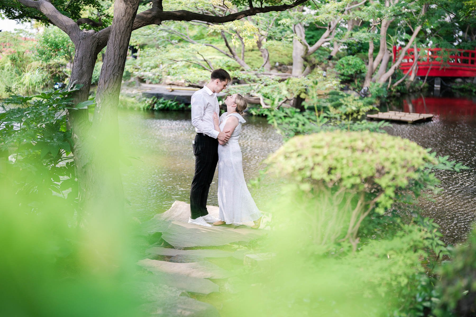 Couple having a romantic moment with a red bridge in the background at a traditional Japanese garden