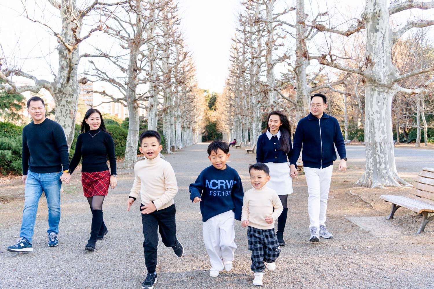 Family with children running down a bare tree-lined avenue during a winter Tokyo photoshoot