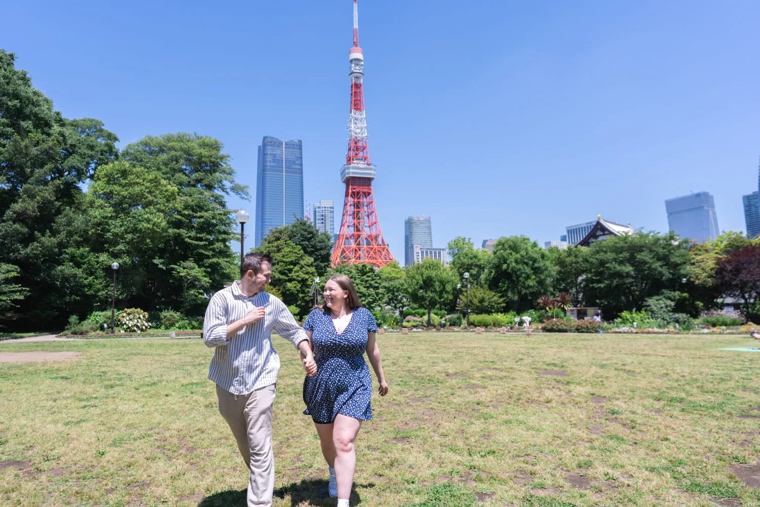 Tokyo photographer captured a candid moment of a couple running while holding hands at Shiba Park with Tokyo Tower in the background