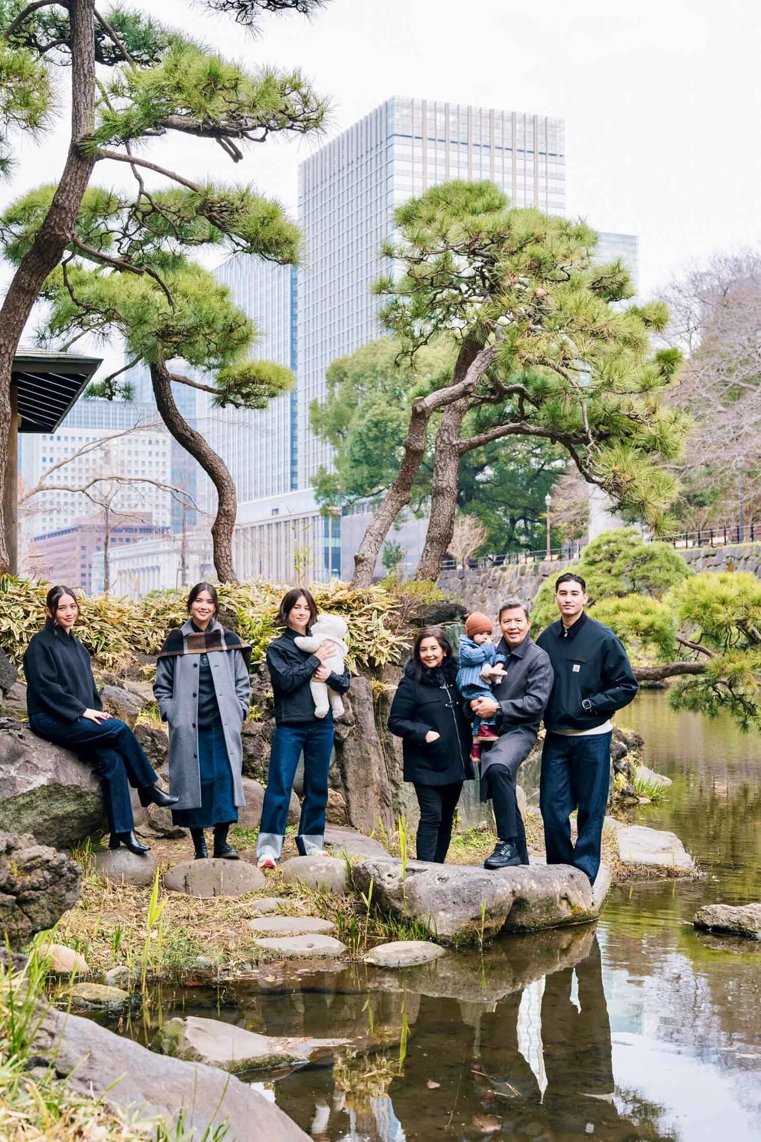 Family portrait among pine trees and a pond at Hibiya Park with the Tokyo skyline behind