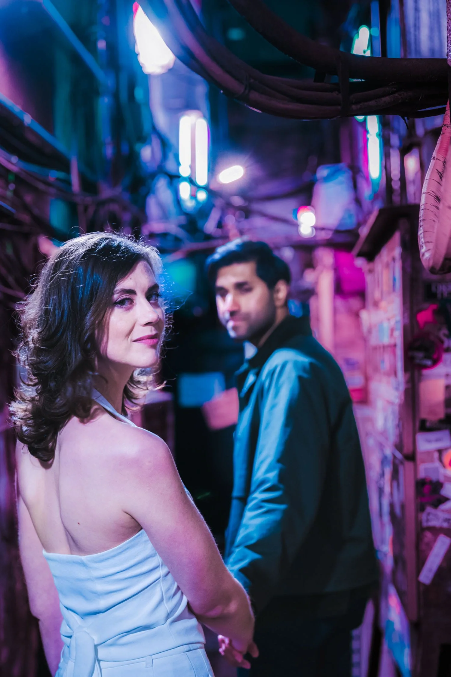 Couple exploring a romantic, dark alley in Golden Gai, Shinjuku, Tokyo surrounded by cinematic cyberpunk-like, pink and blue neon lights.