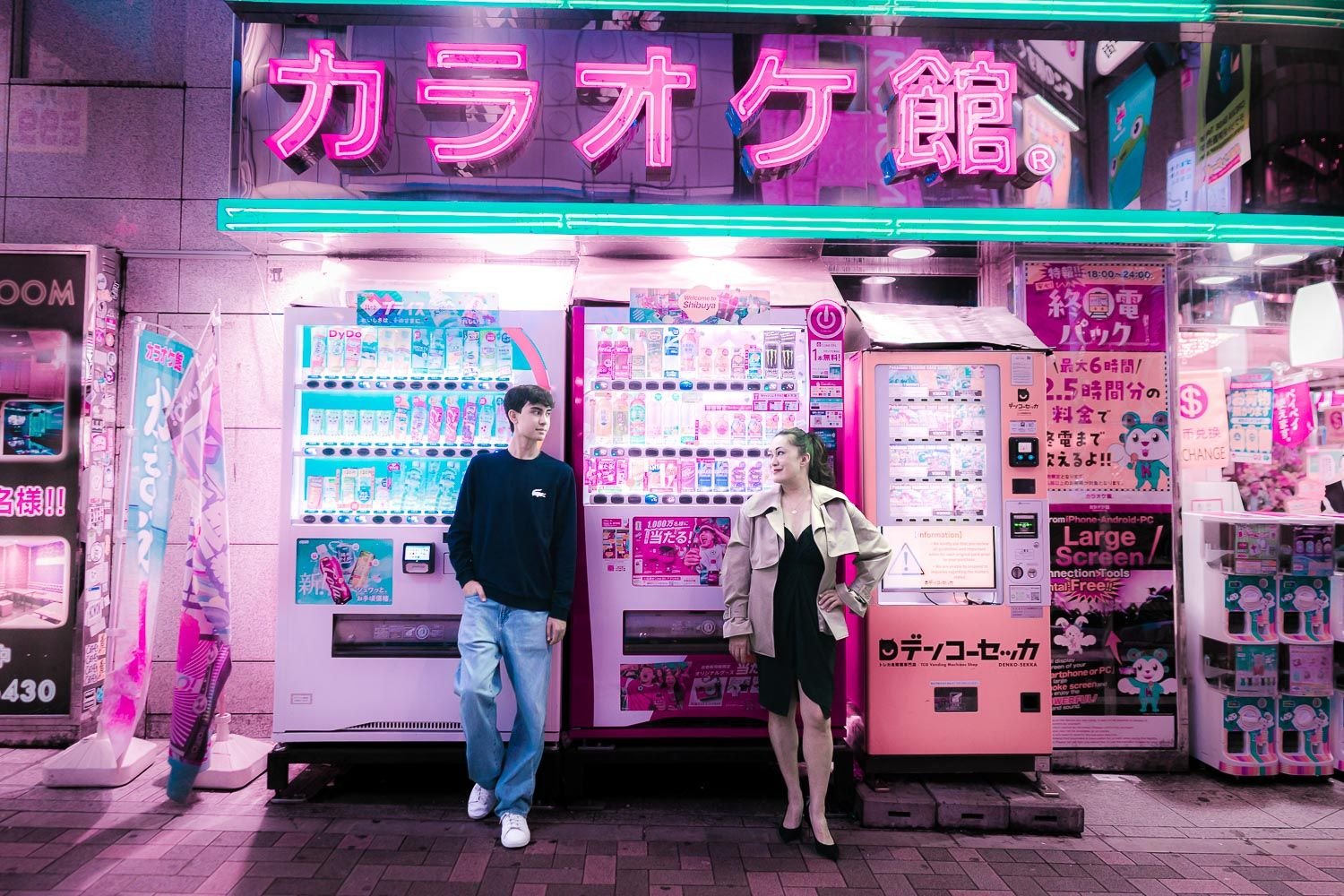 Mother and son leaning on colorful vending machine and neon signs in Shibuya, Tokyo, with vibrant pink and turquoise cyberpunk-style lighting.