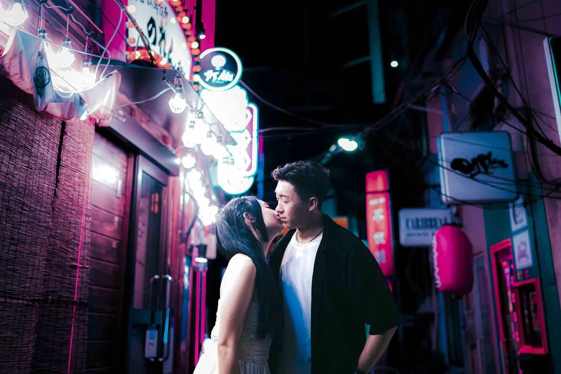 Couple kissing in a neon-lit Tokyo alley in Kabukicho, Shinjuku, surrounded by vibrant pink, blue, and purple lights and Japanese signs.