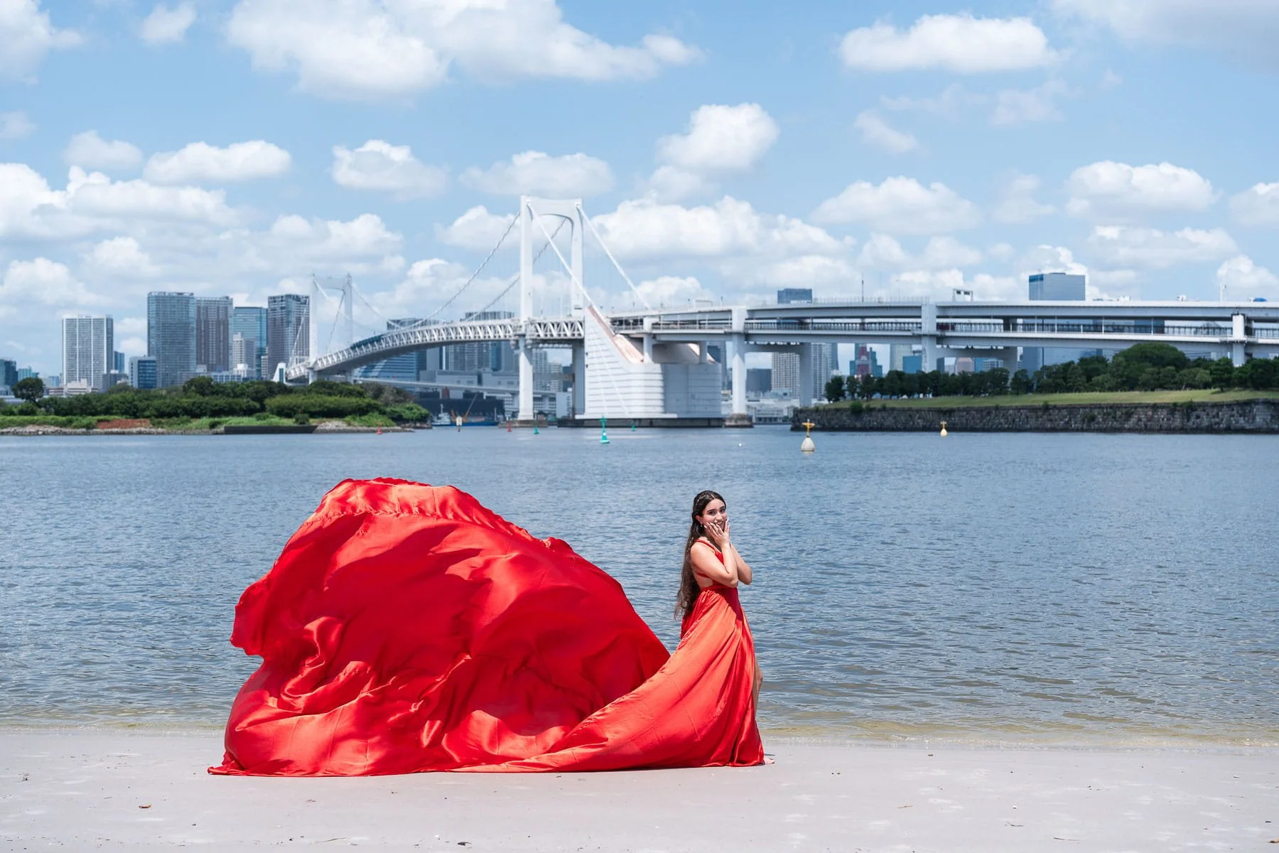 Quinceañera in a flowing red gown on the beach with Rainbow Bridge and Tokyo Bay in the background