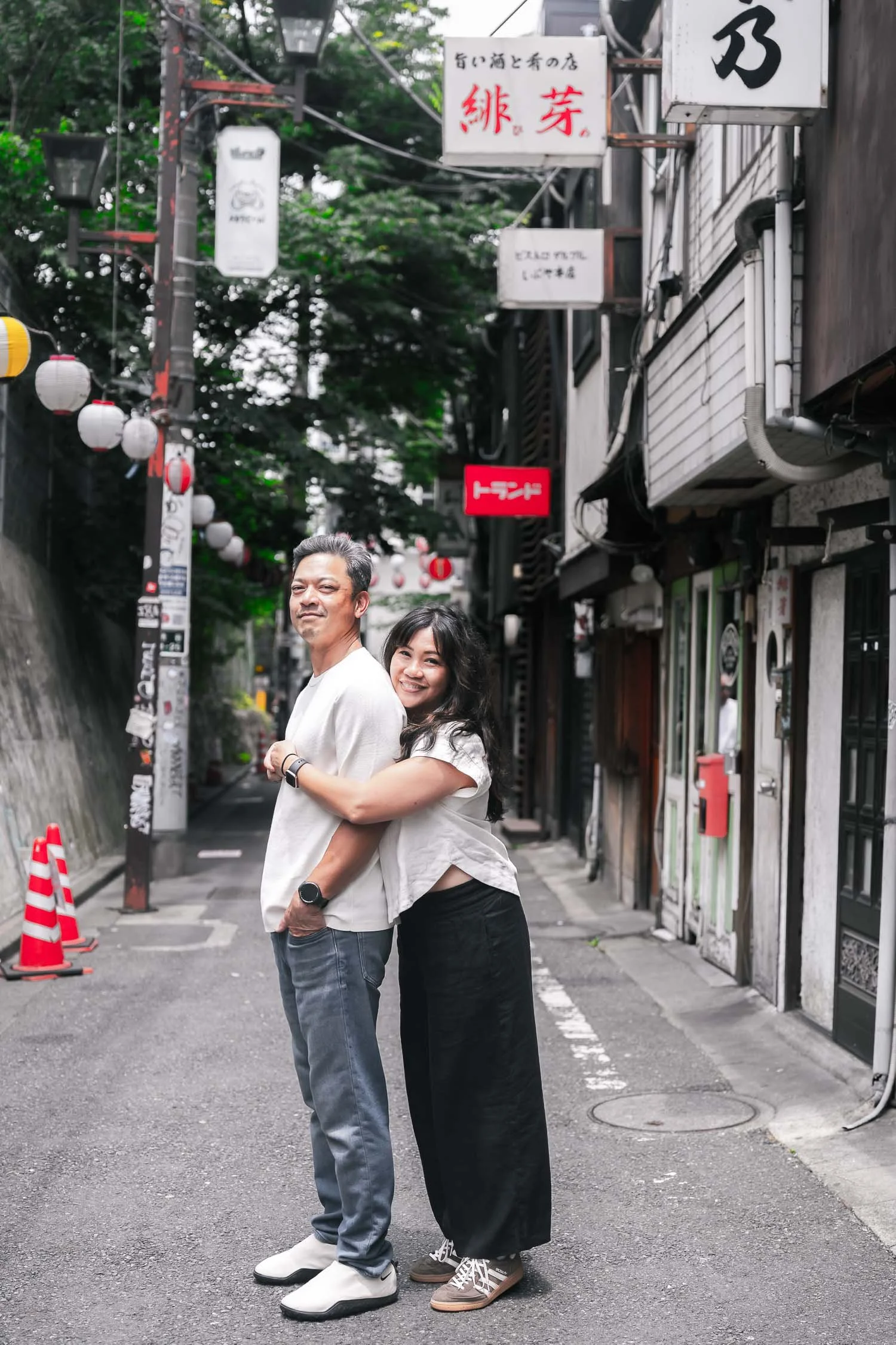Couple embracing on a quiet Tokyo backstreet lined with izakaya signs and paper lanterns