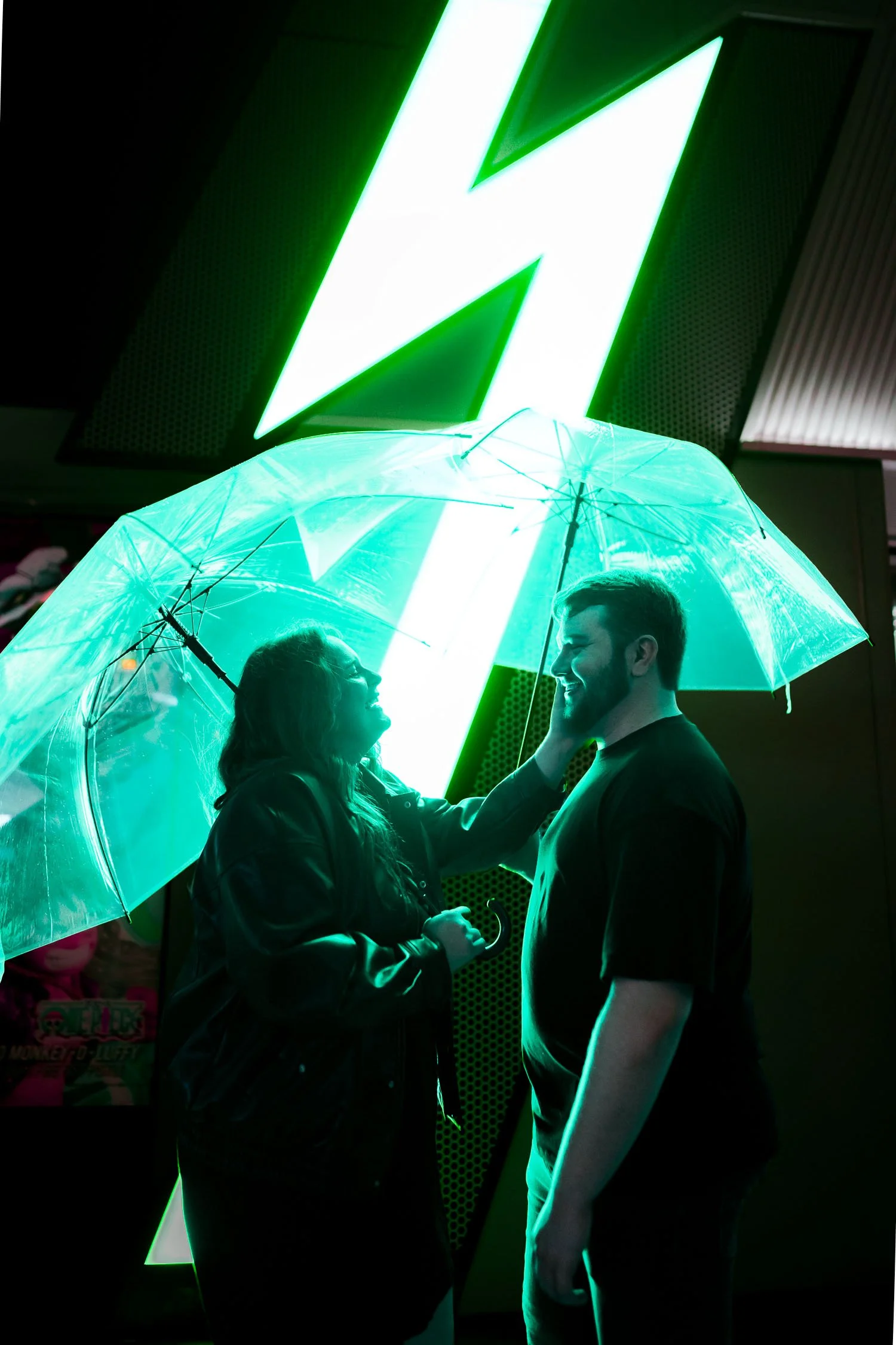 Couple sharing an intimate moment under a clear umbrella lit green by neon signage in Akihabara, Tokyo