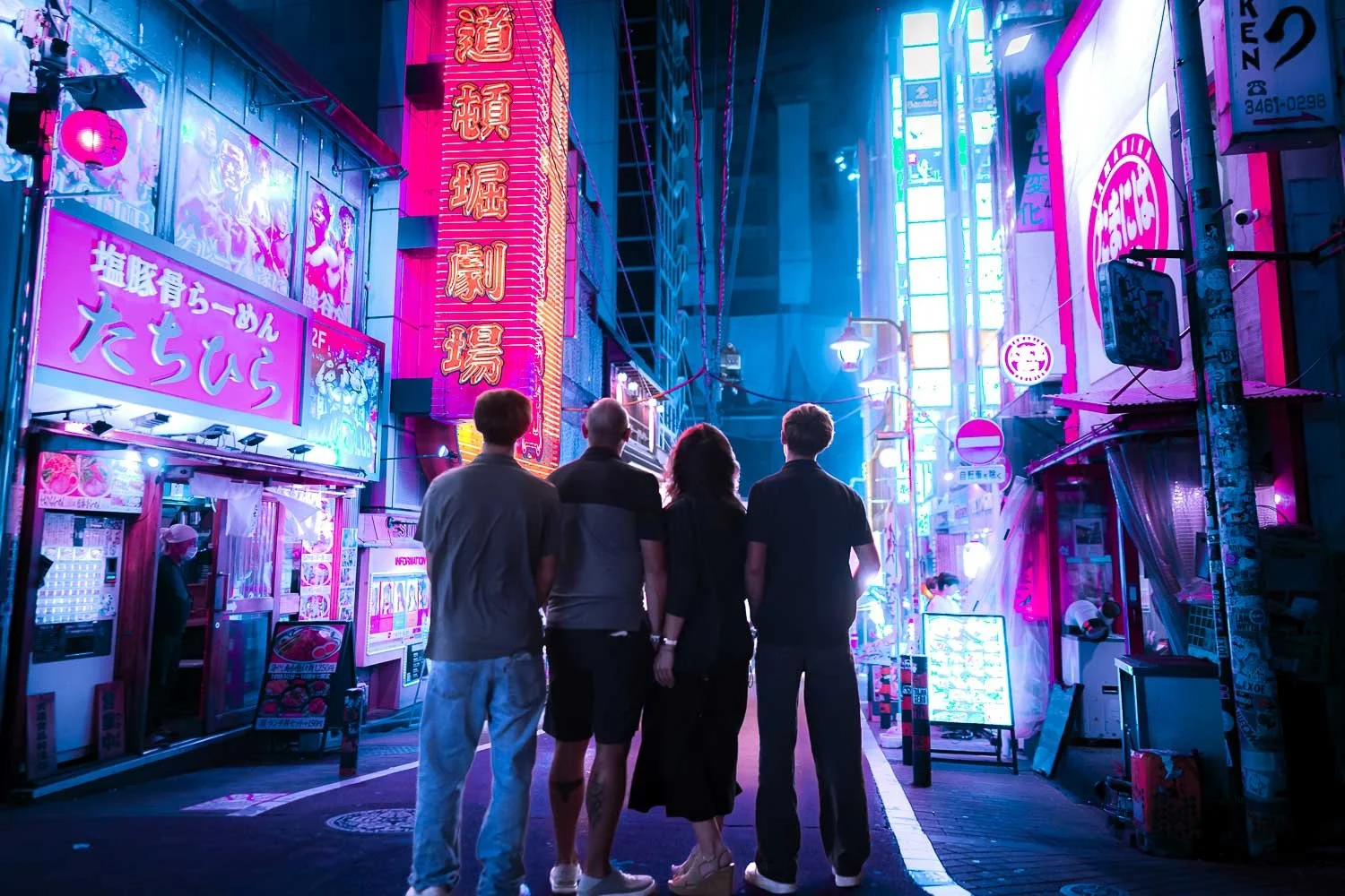 Family of four standing together in a neon-lit Tokyo alley during a cyberpunk-style photoshoot