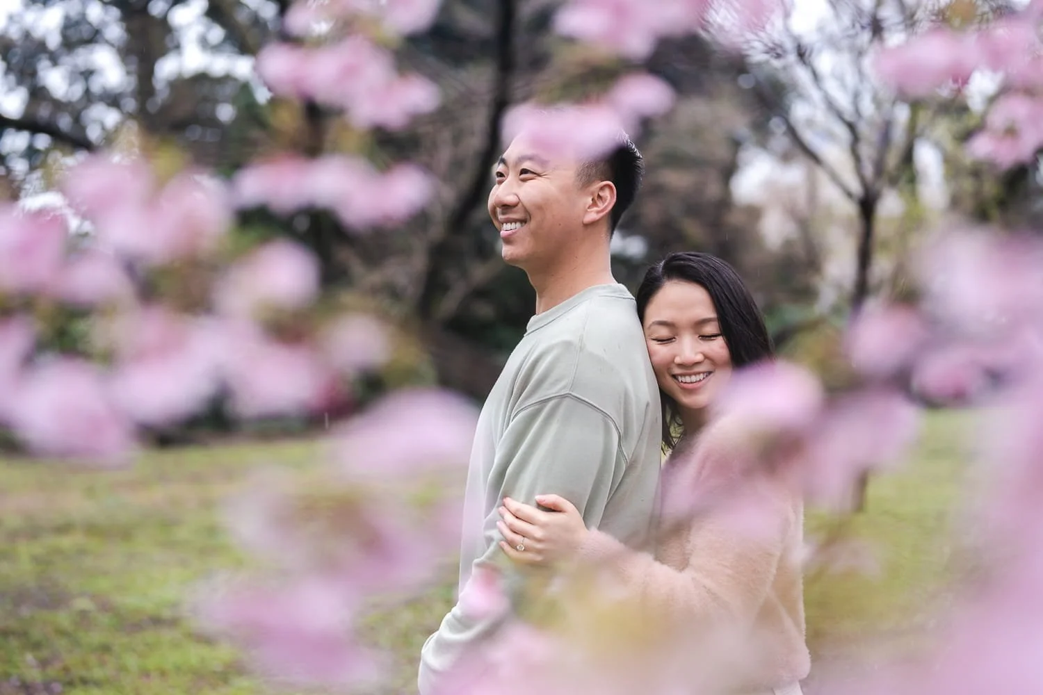 Tokyo surprise proposal photographer captured a couple standing next to pink sakura flowers hugging and smiling.