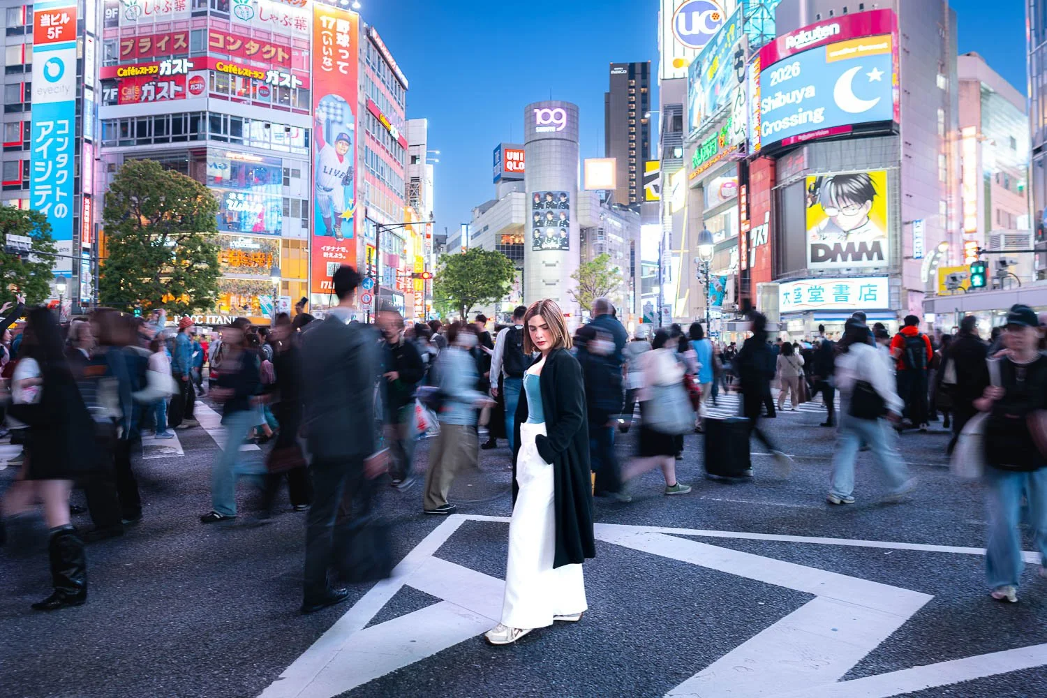 Solo female traveler stops in the middle of Shibuya Scramble Crossing while other pedestrians passing by as the time stops. Captured by KP Photography, English- speaking professional Tokyo photographer