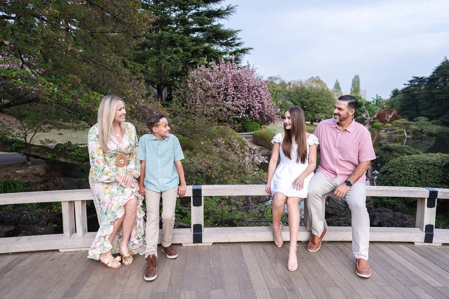 Family resting while sitting for a conversation on the wooden bridge with sakura in the background.