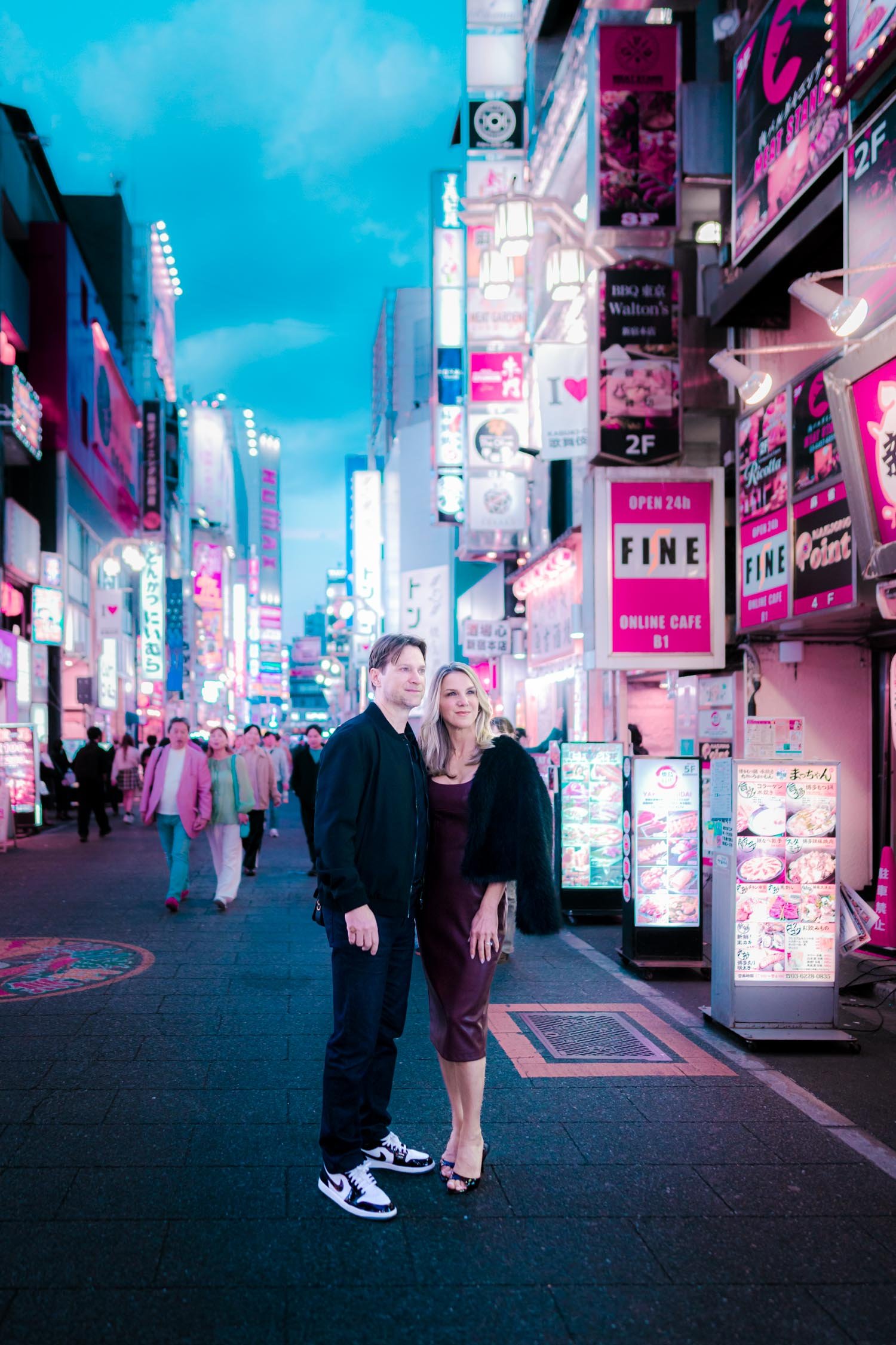 Couple standing in Kabukicho, Tokyo, at dusk surrounded by neon signage in a cyberpunk-style photoshoot