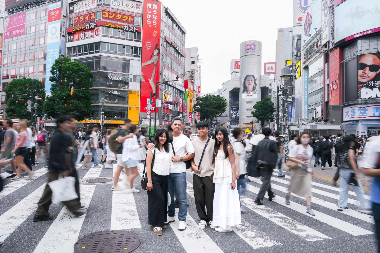 Family of four posing together at Shibuya Crossing with Tokyo's neon billboards behind them