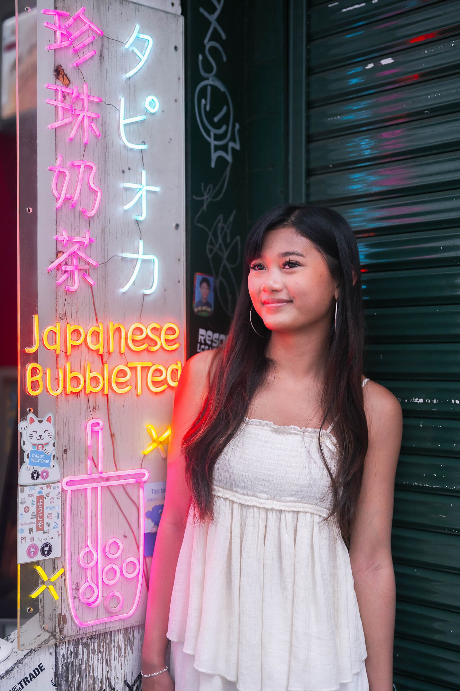 Young woman smiling beside a glowing Japanese bubble tea neon sign in Shibuya, Tokyo
